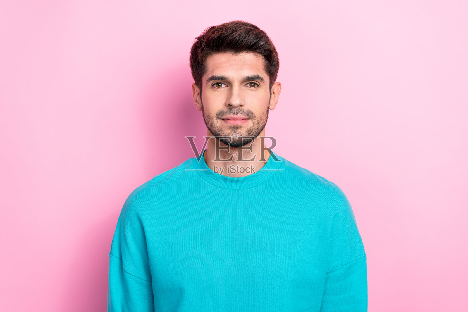 时尚蓝色服装的迷人年轻男子，冷静自信地看着镜头，背景为粉色。照片摄影图片