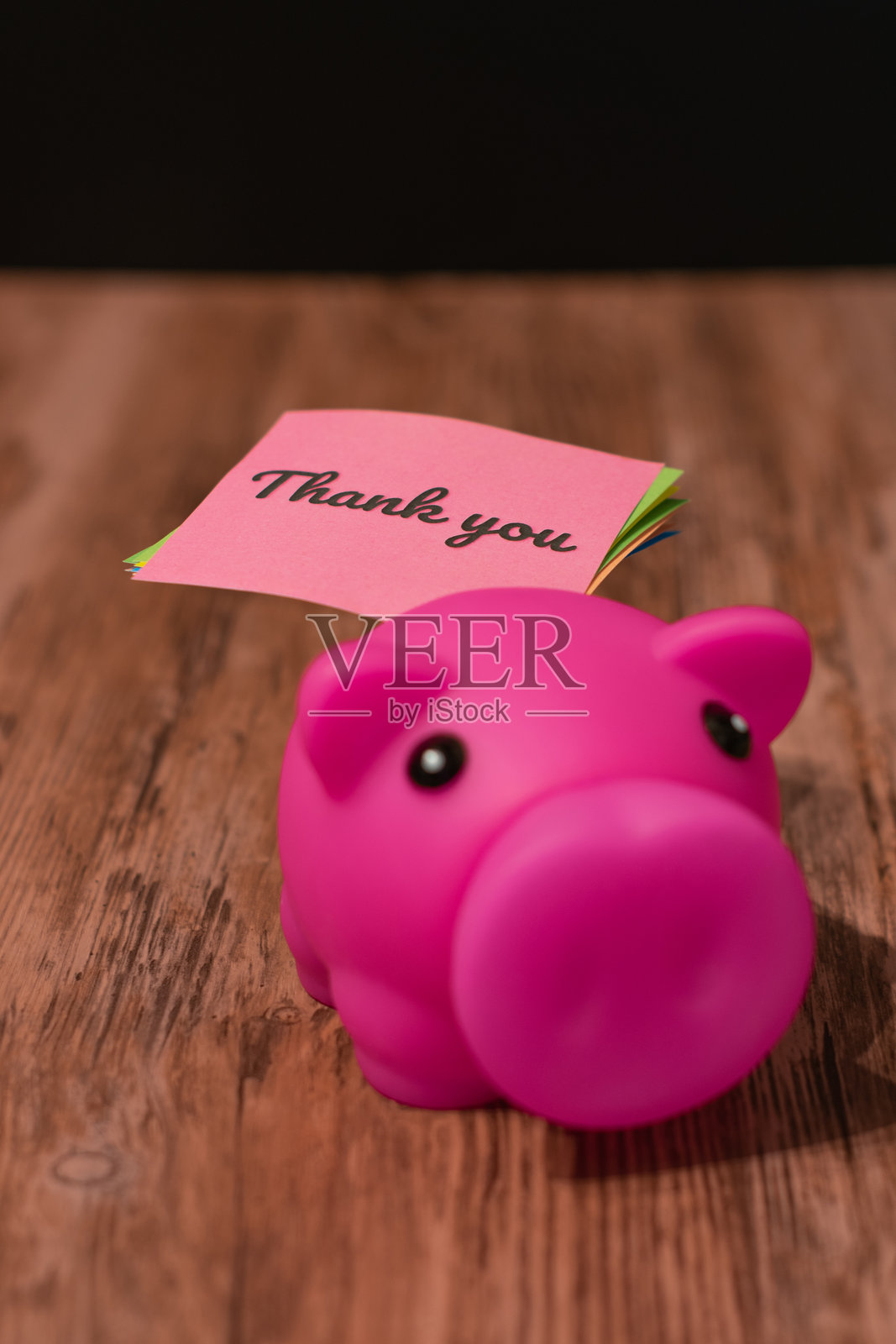放在木质表面黑色背景的粉色感谢便条和储蓄罐照片摄影图片
