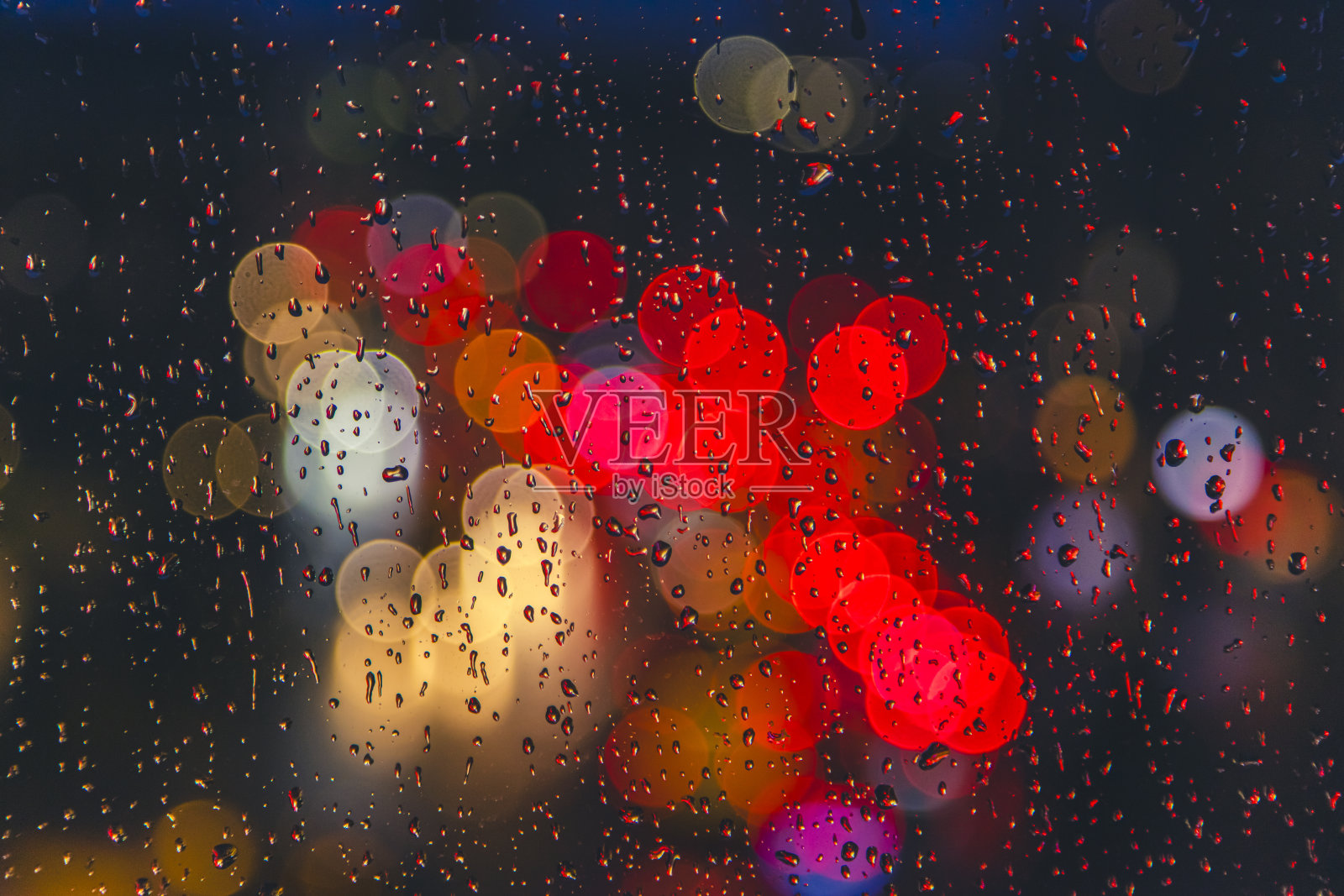 窗户表面上的雨滴与背景中五光十色的交通虚化灯光照片摄影图片