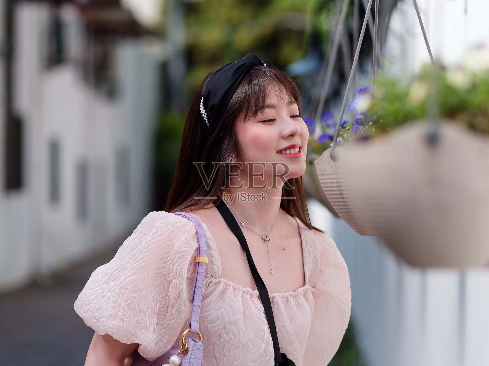 美丽的年轻中国女性在阳光明媚的夏日中享受花香，穿着可爱的粉色裙子。情感、人物、美丽、青春和生活方式的肖像，街头摄影。照片摄影图片