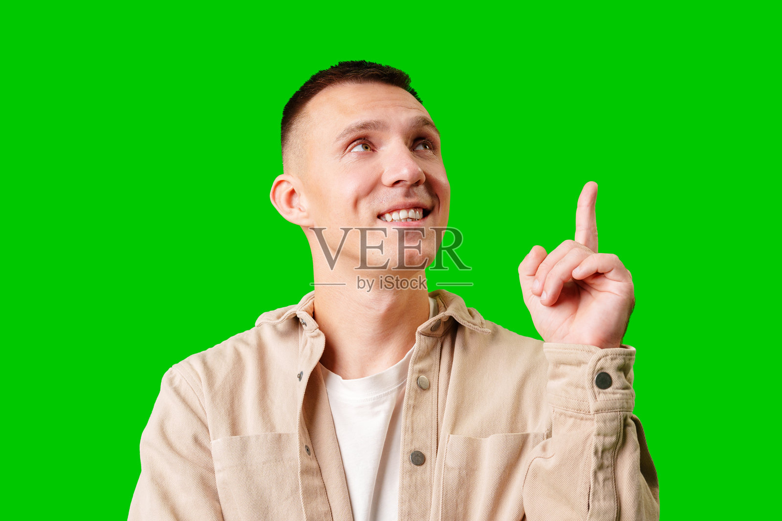 年轻男人在亮绿色背景下微笑并向上指照片摄影图片