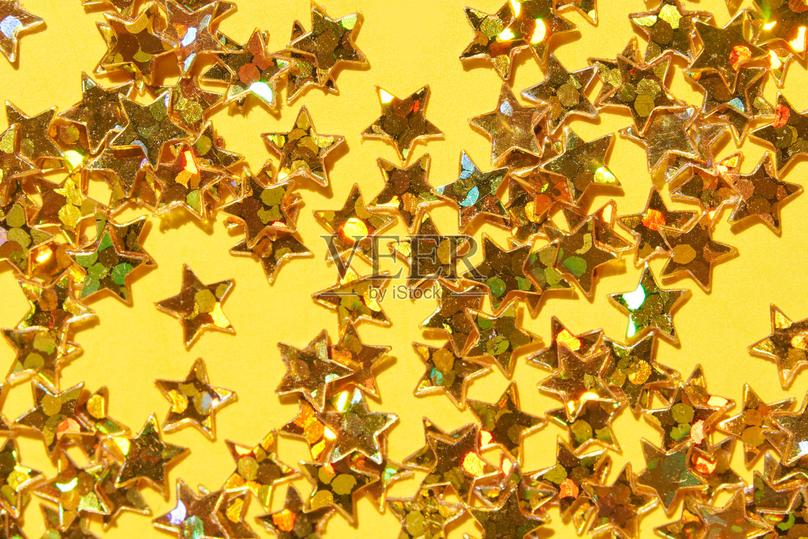 闪亮的金色星星彩纸屑在生动的黄色背景上，适合节日庆祝。照片摄影图片