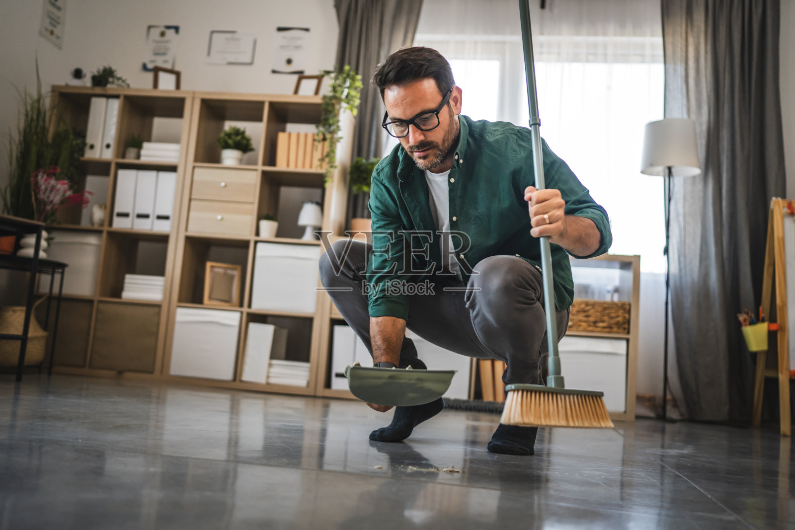 成年男子用扫帚和簸箕清理地上的破花瓶碎片照片摄影图片