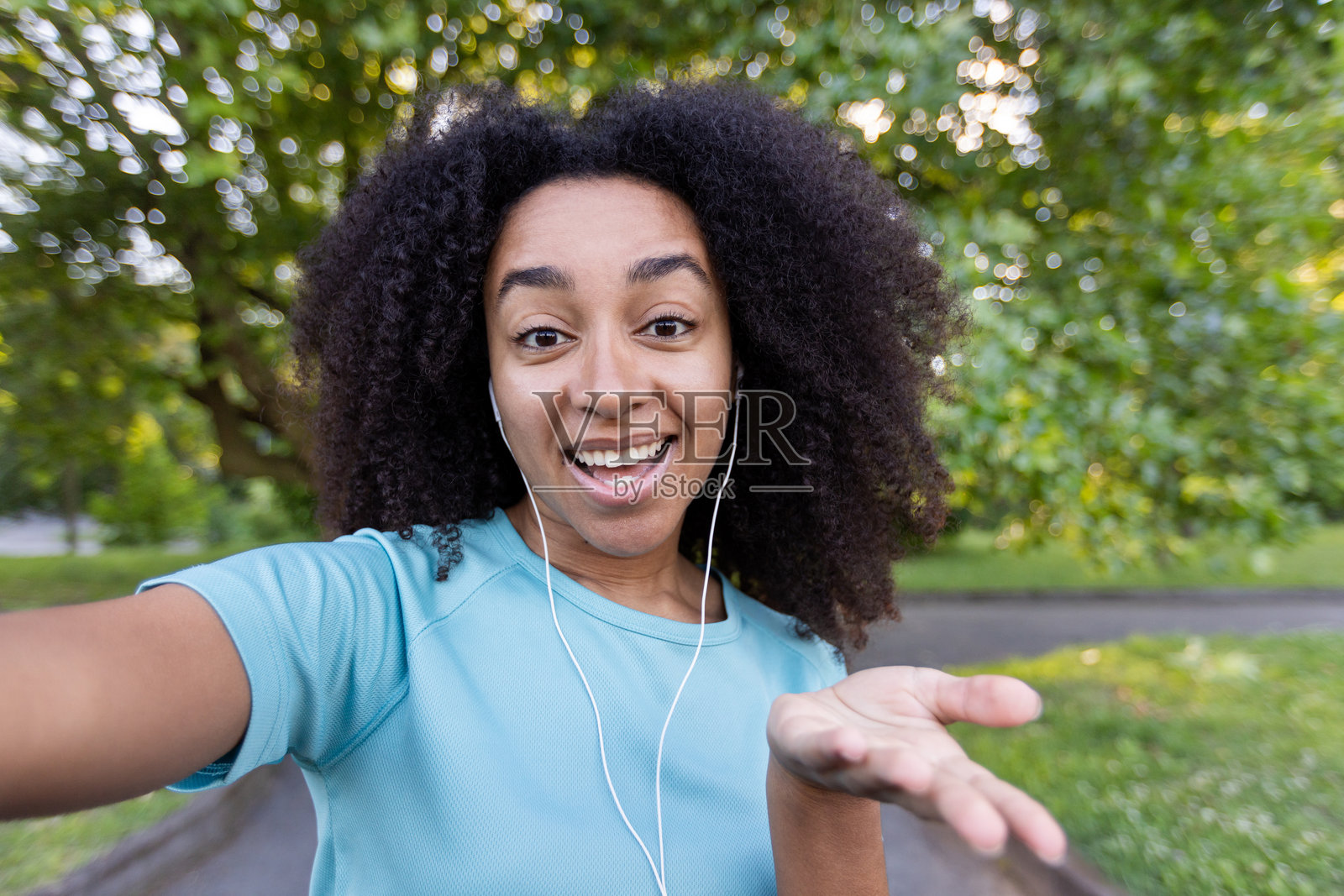 快乐的女人在公园里通过手机进行视频通话健身，穿着休闲运动服和耳机，背景是生机勃勃的绿色自然照片摄影图片