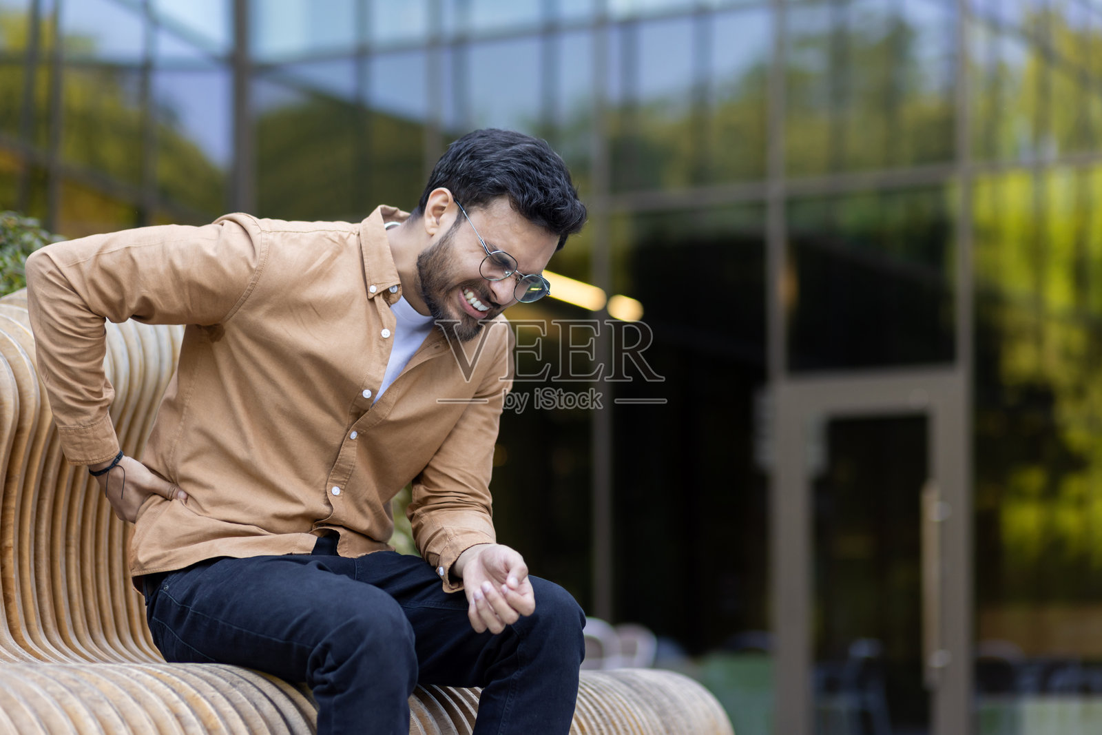 男子坐在城市中的户外长椅上，感到背痛照片摄影图片