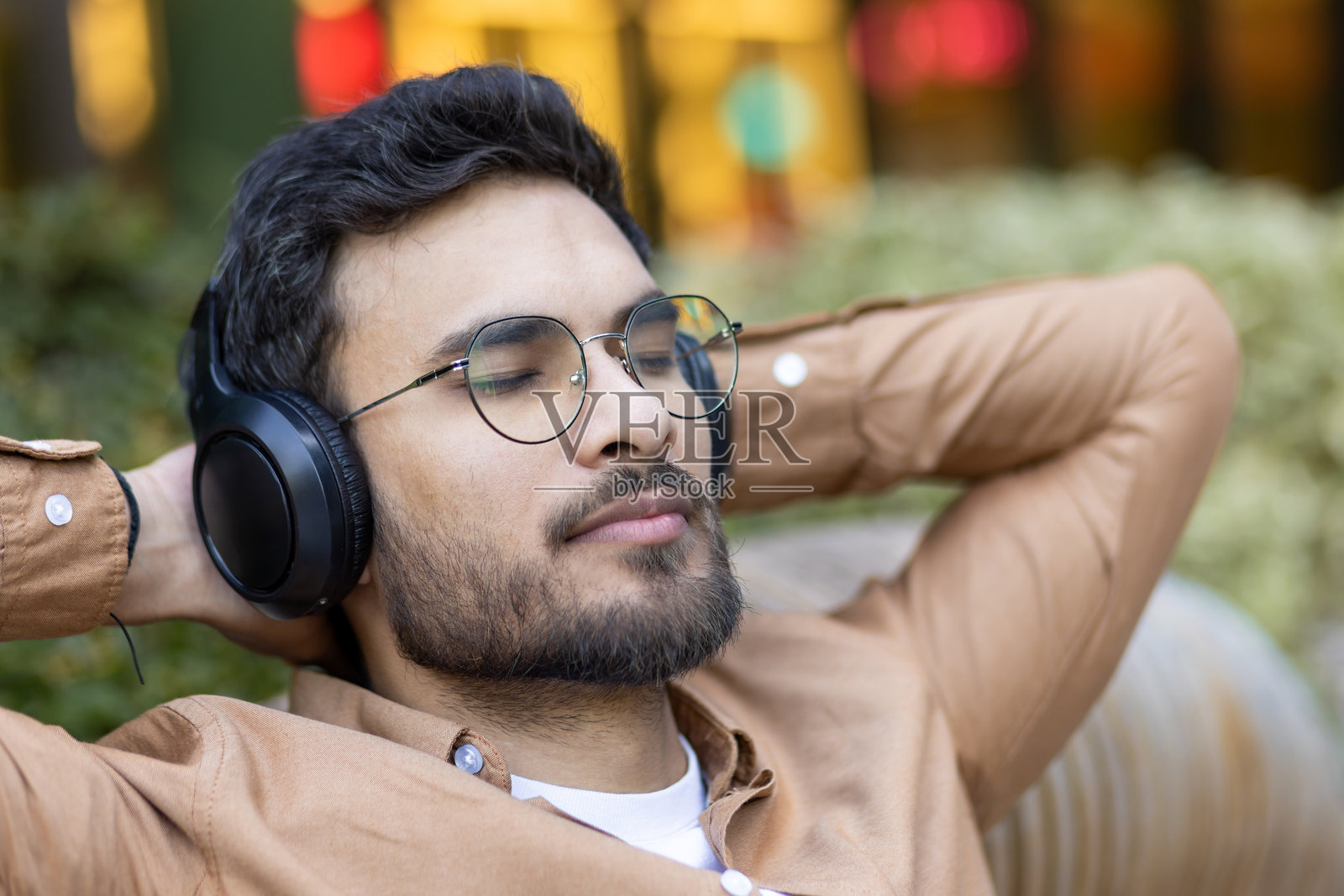 年轻男子在城市公园的户外环境中，戴着耳机享受音乐和放松时光。照片摄影图片