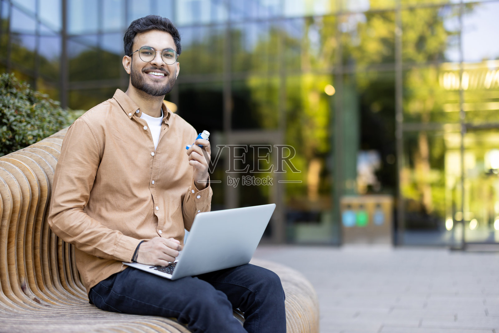 快乐的男人在户外使用笔记本电脑，拿着哮喘吸入器，在城市环境中休息照片摄影图片