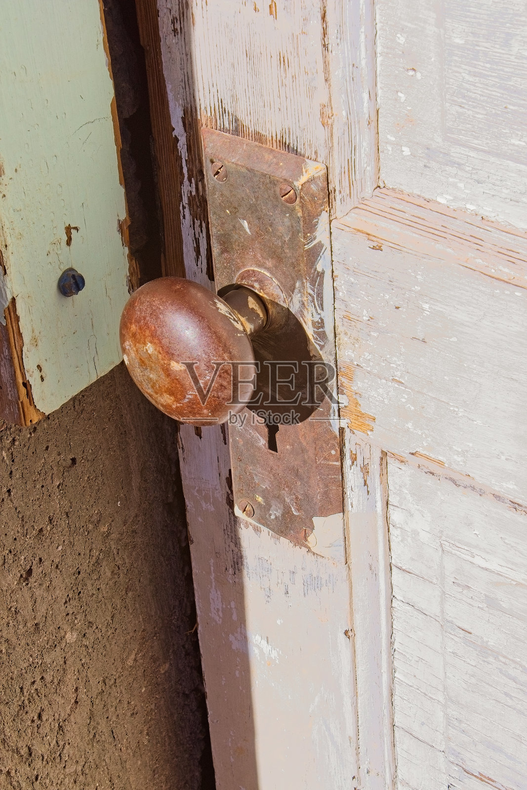 一扇老旧的白色木门上的生锈门把手，门面涂层开裂。照片摄影图片