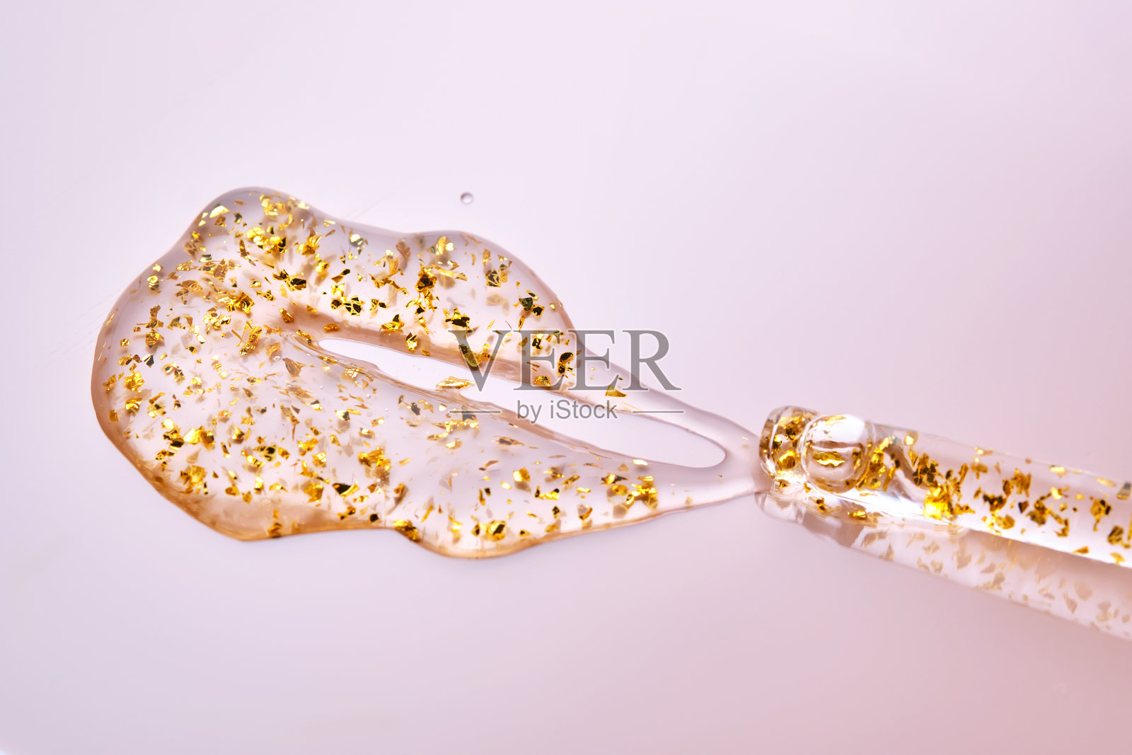 粉色背景上的24K黄金精华滴管。照片摄影图片