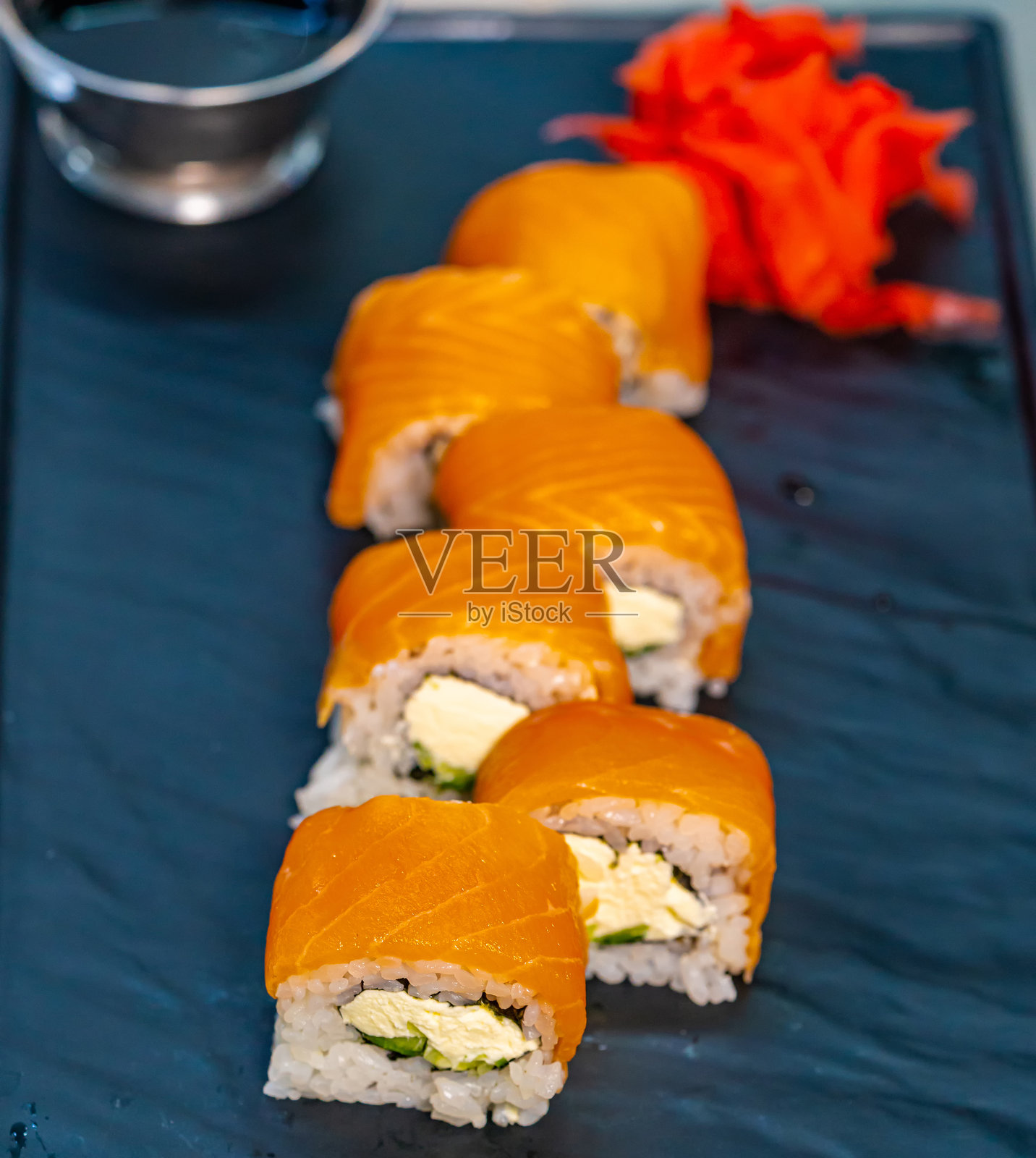 一个蓝色托盘上放着寿司，旁边有一碗酱汁。美味的寿司拼盘配上香浓的酱汁，摆放在鲜艳的蓝色托盘上。照片摄影图片