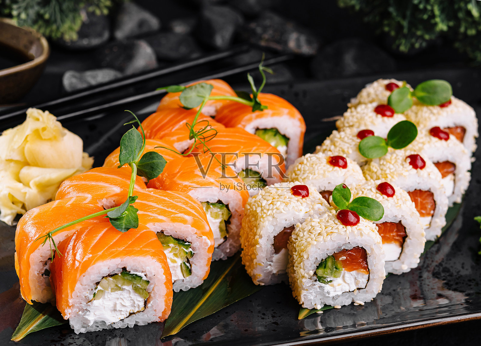 两种配有三文鱼和芝麻的寿司卷，摆放在黑色盘子上照片摄影图片