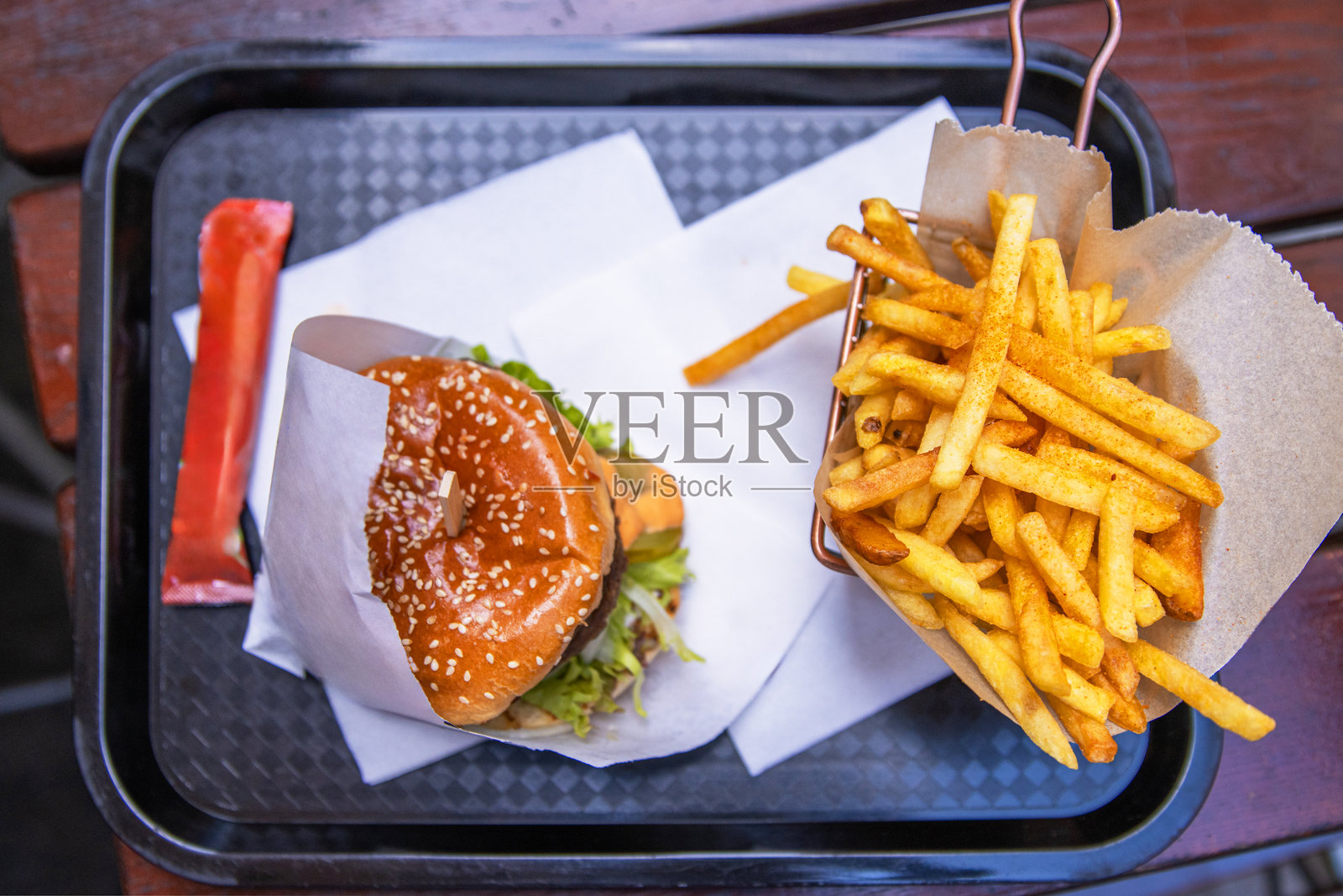 一个双层汉堡，上面有生菜和酱汁，旁边配有脆脆的薯条，放在快餐店桌子上的托盘里。新鲜制作的奶酪汉堡配上金黄色的薯条。俯视图。照片摄影图片