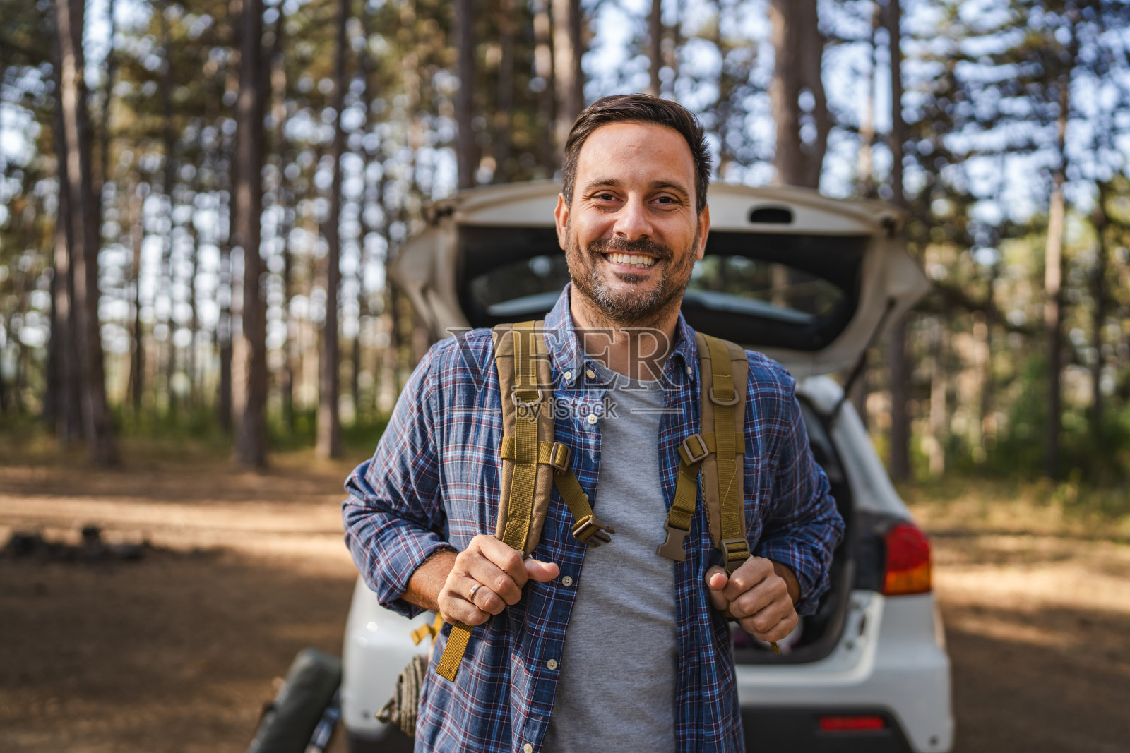 成年男性露营者在森林中站在汽车前，手持背包的肖像照片摄影图片