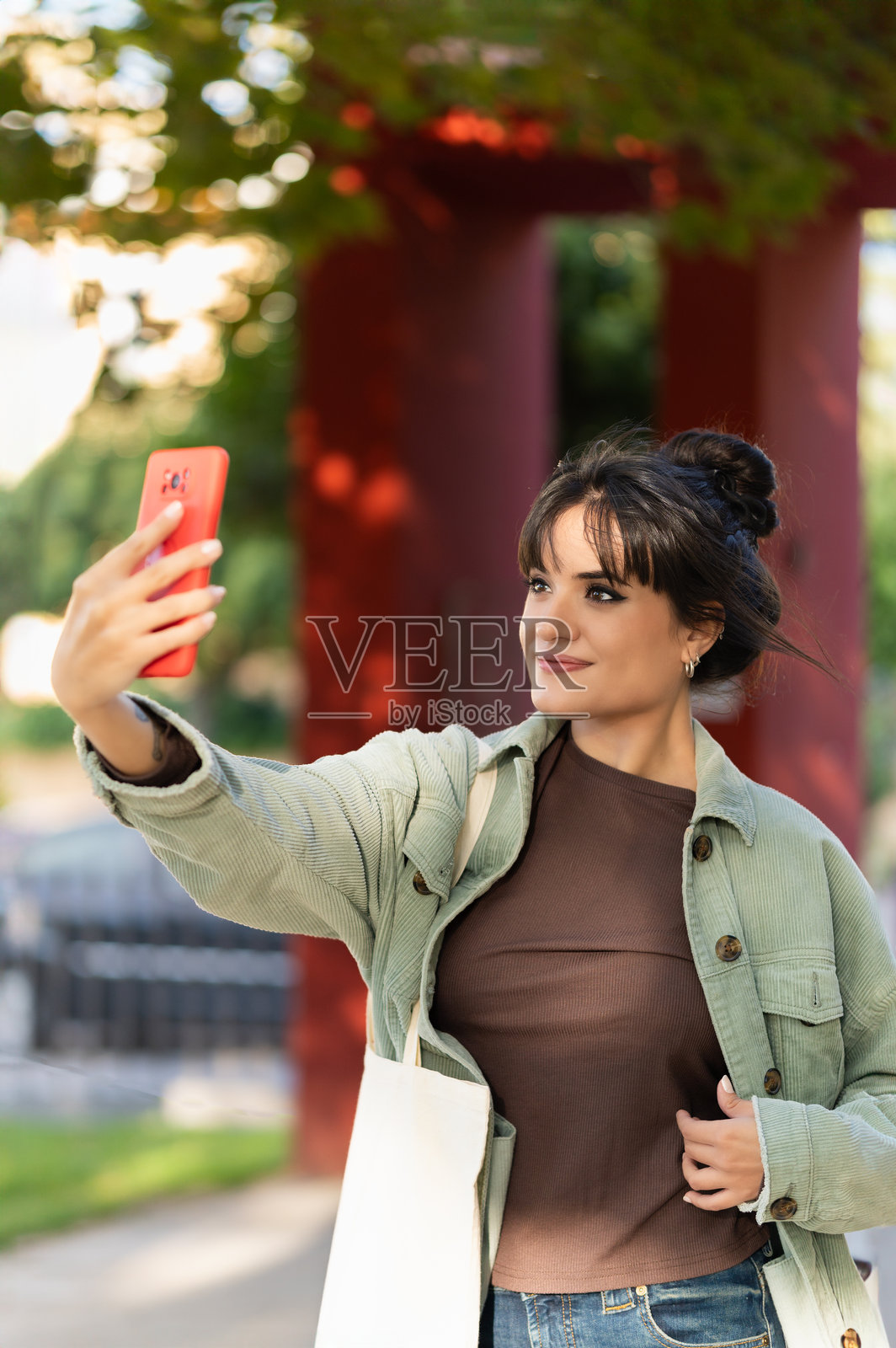 女人在户外用红色手机微笑拍照。生活方式概念照片摄影图片