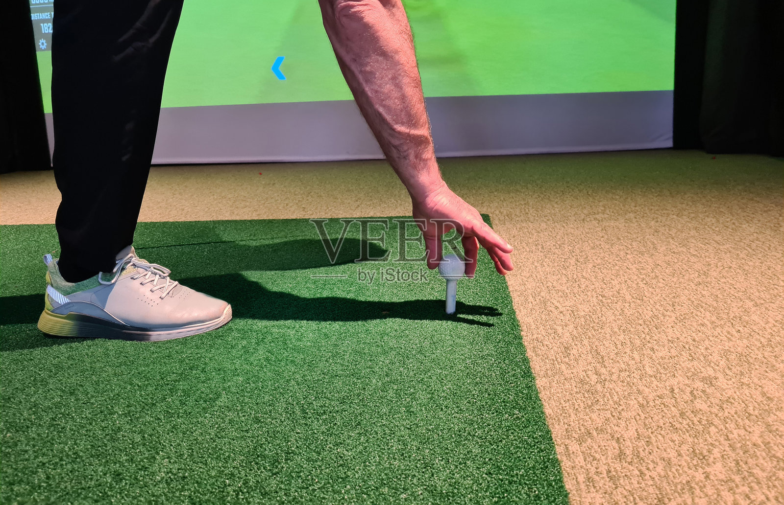 高尔夫球手在室内人造草皮上摆放高尔夫球，专注于握杆照片摄影图片