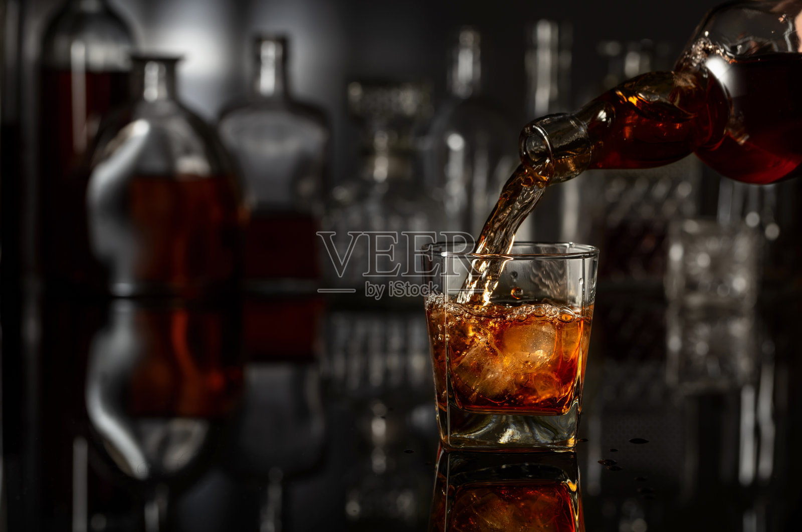 从瓶子倒入装有冰块的威士忌酒杯照片摄影图片