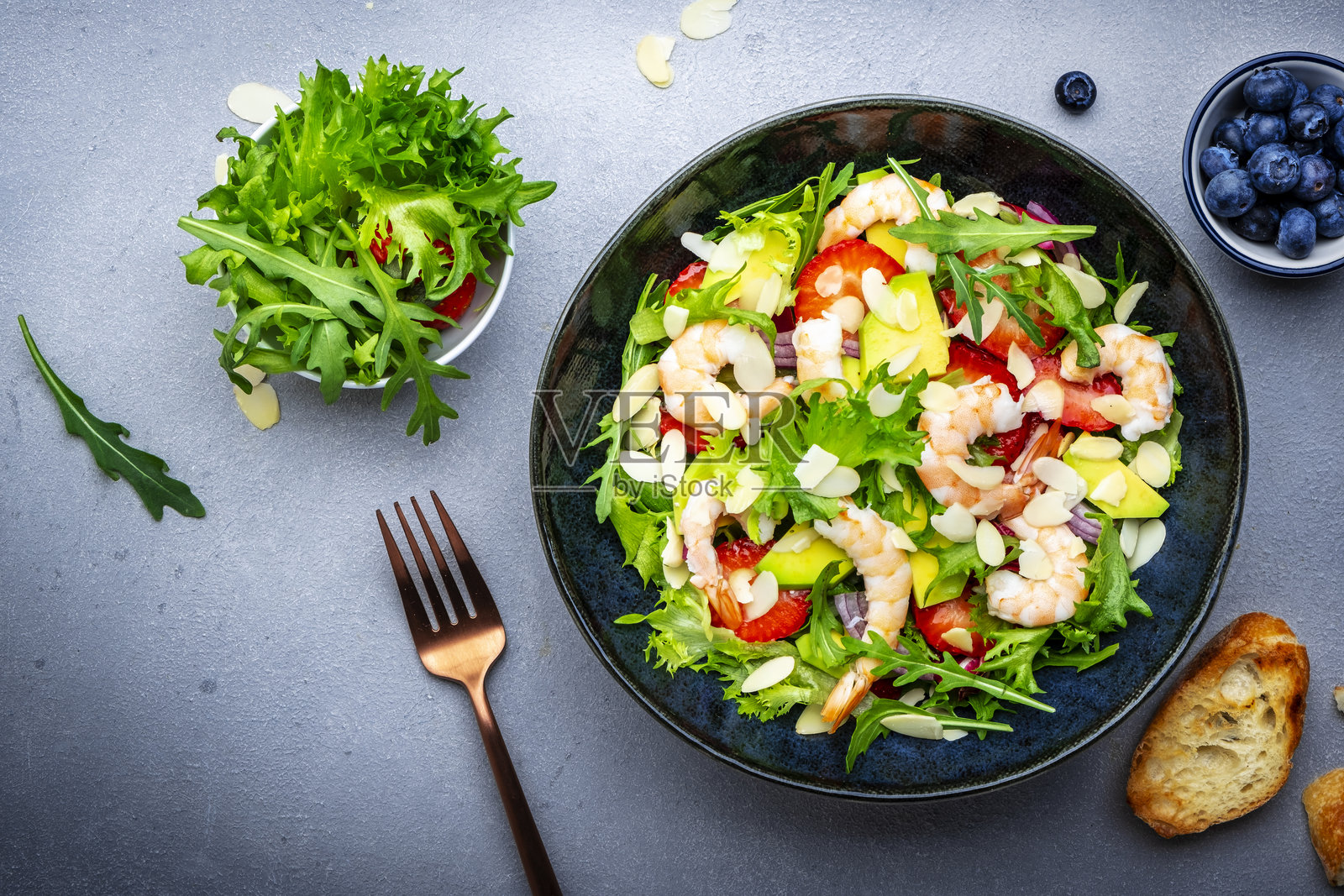 美食爱好者的沙拉，配有虾、草莓、洋葱、芝麻菜和杏仁片，灰色背景，俯视图照片摄影图片