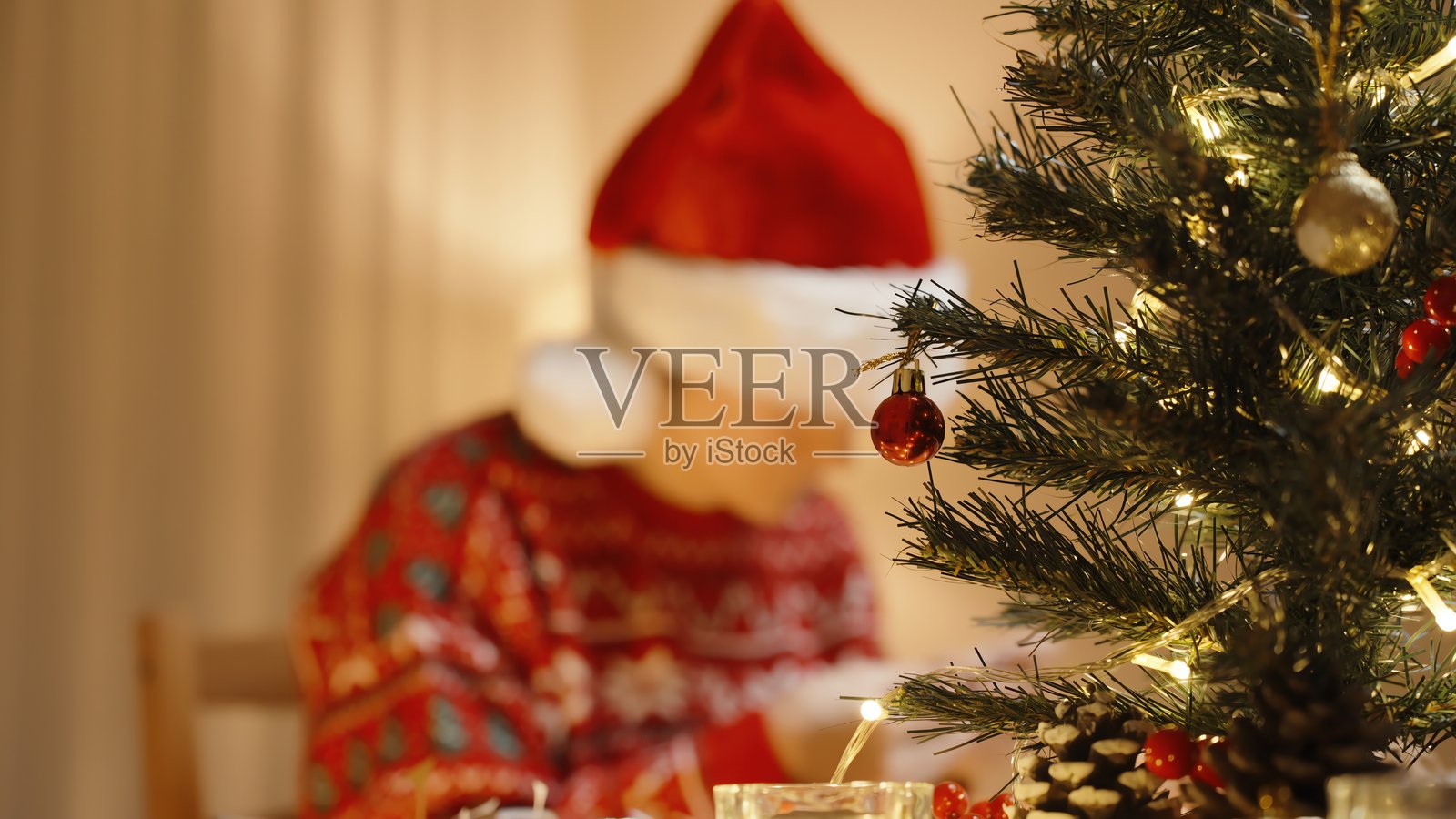 前景为圣诞装饰树，背景为戴圣诞帽的女士在节日气氛中制作工艺品照片摄影图片