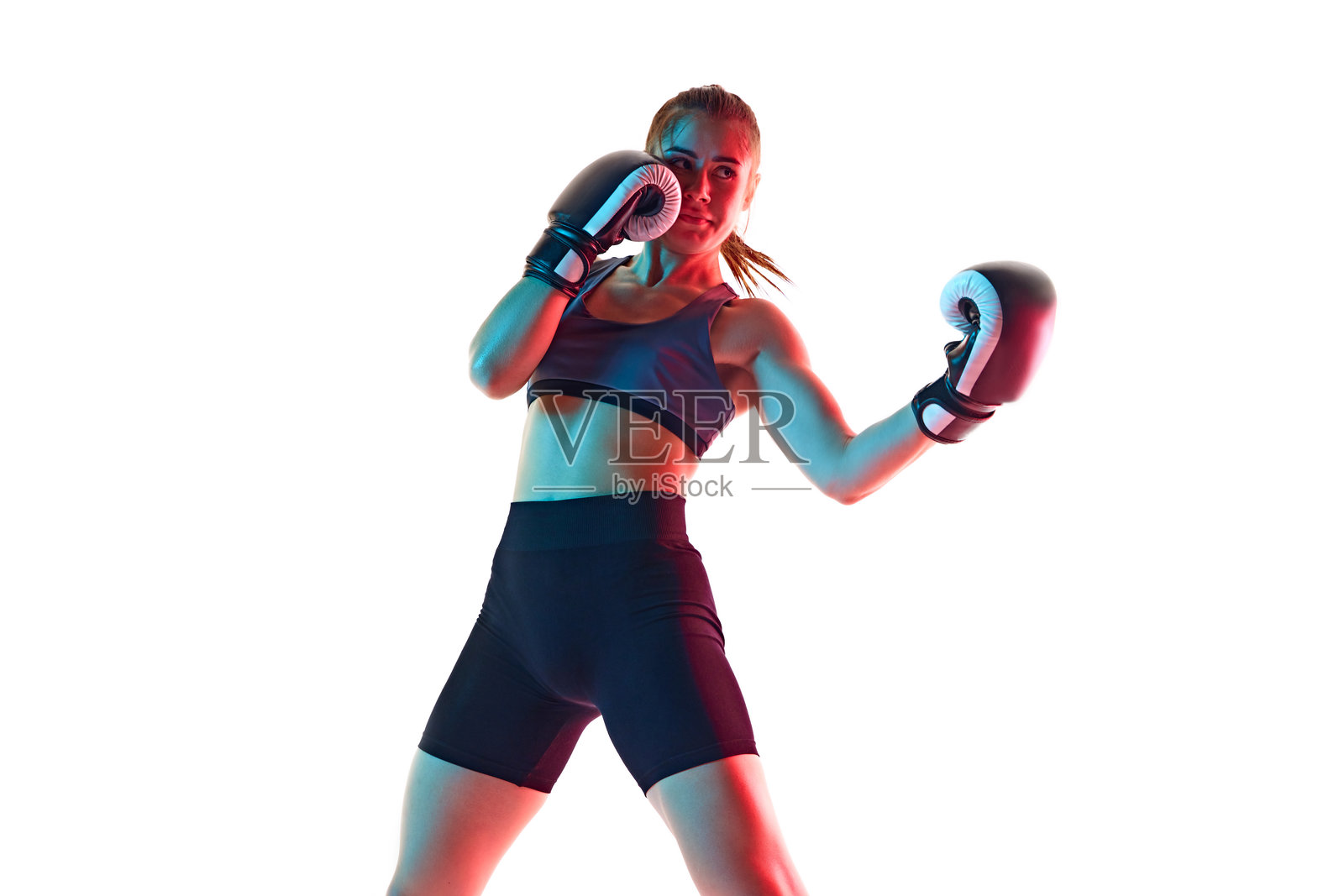 上勾拳。集中精力、身材健美的年轻女子，拳击运动员在霓虹灯下的白色工作室背景中训练照片摄影图片