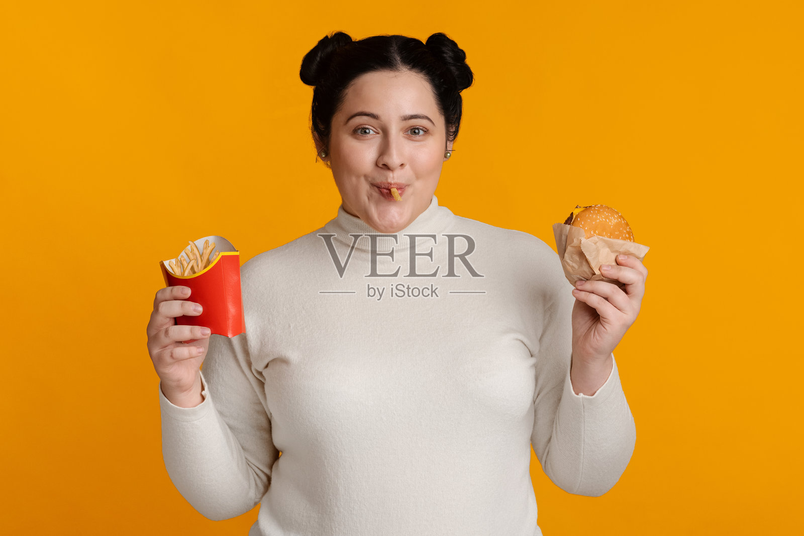 黄色背景上吃汉堡和炸薯条的滑稽胖女孩照片摄影图片
