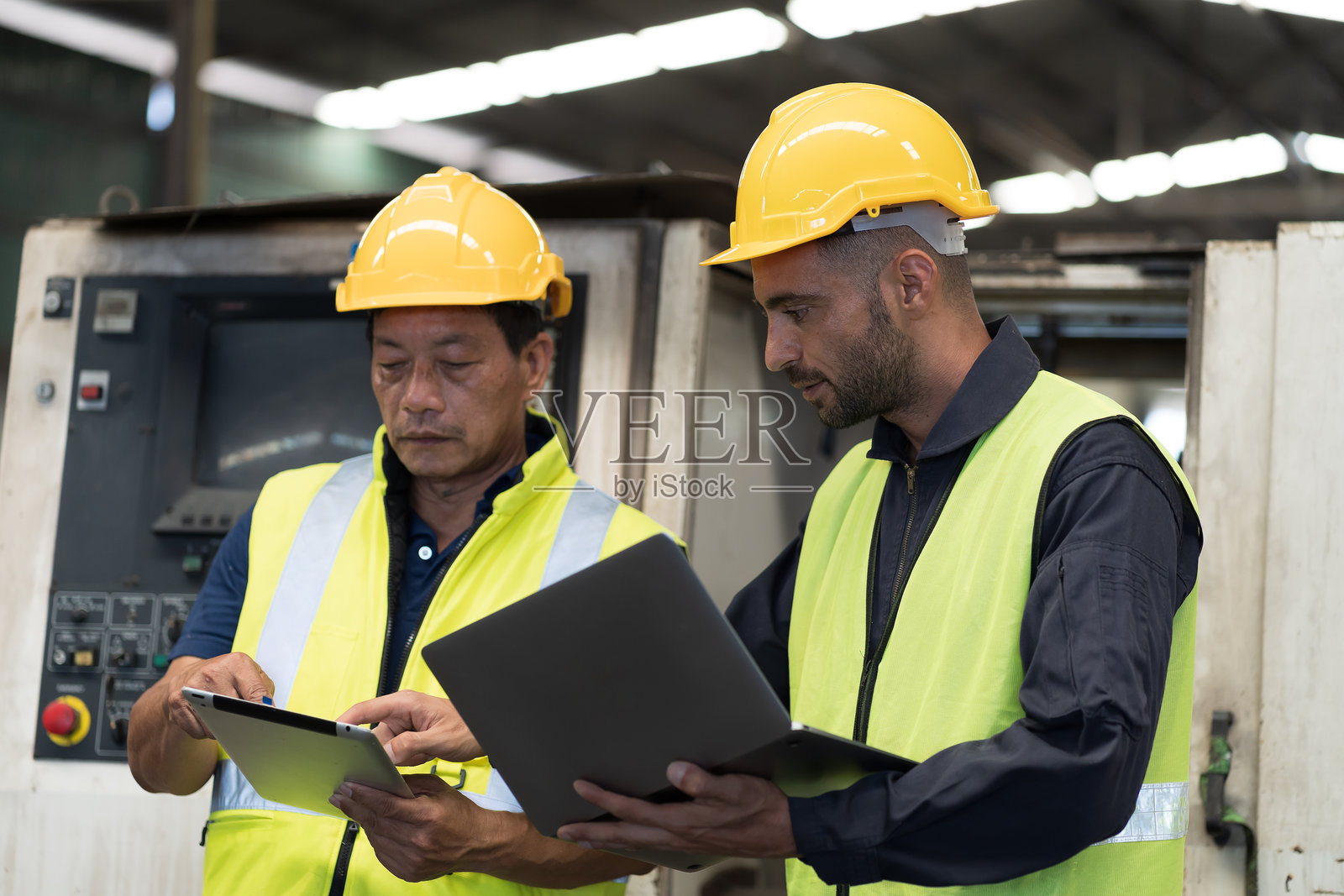 两名男性工程师在工业工厂中讨论并合作。一名男性工程师正在工厂中维修或保养数控机床。照片摄影图片