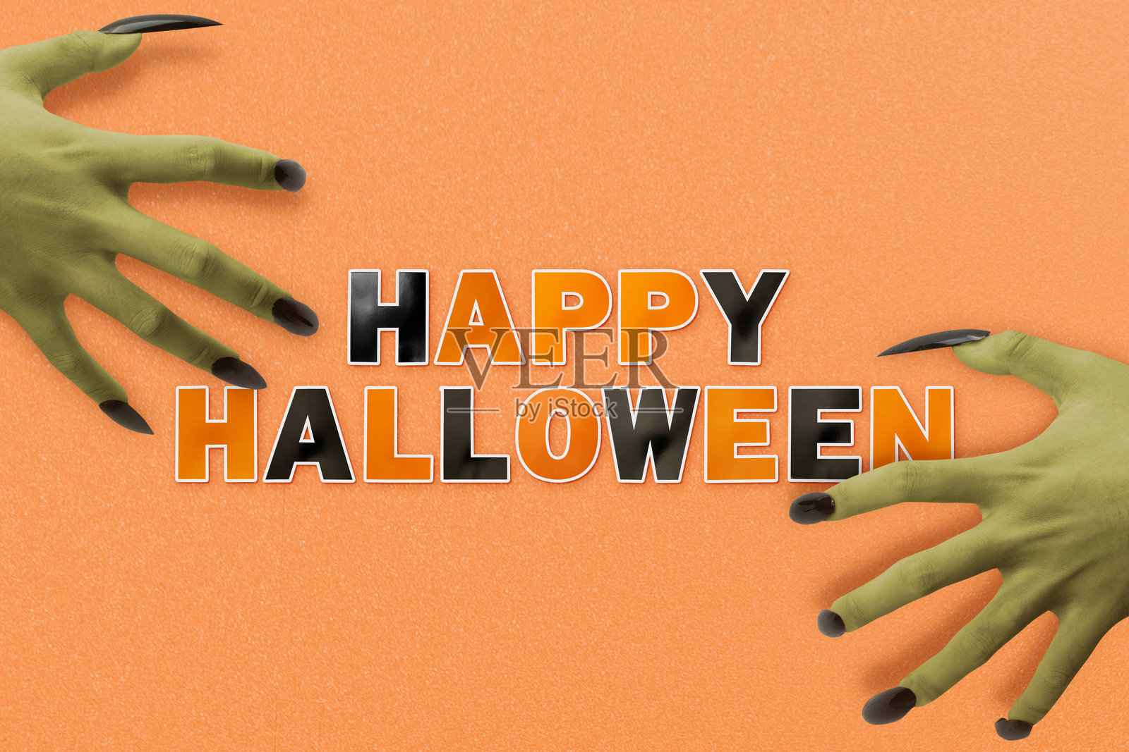 绿色女巫的手指甲修长且为黑色，展示着黑色和橙色字母，写着“万圣节快乐”，背景色彩丰富。照片摄影图片