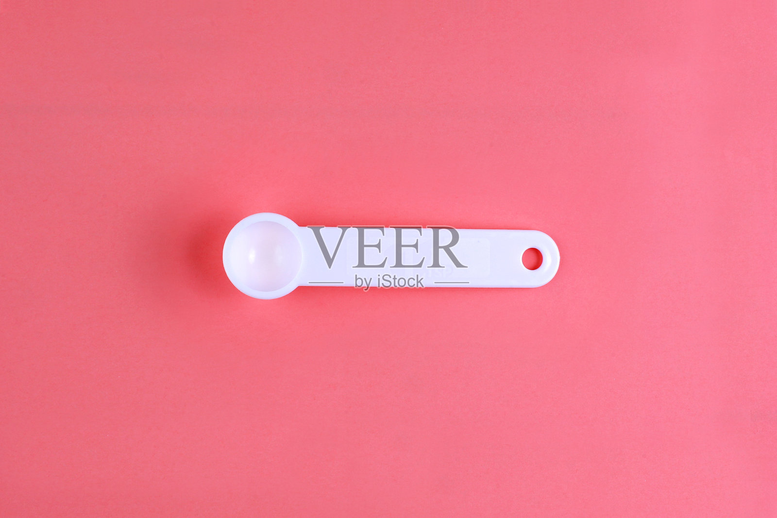 白色塑料勺子特写，背景为珊瑚色照片摄影图片