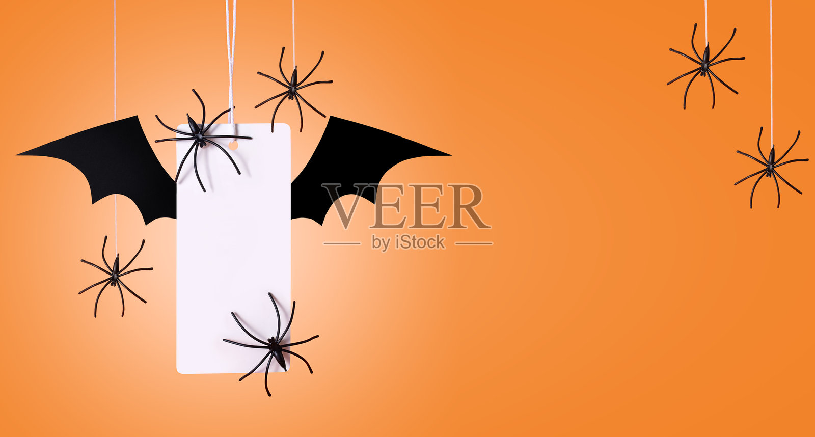 橙色背景上带有蝙蝠翅膀的白色标签，配有蜘蛛。万圣节购物。万圣节概念。横幅。照片摄影图片