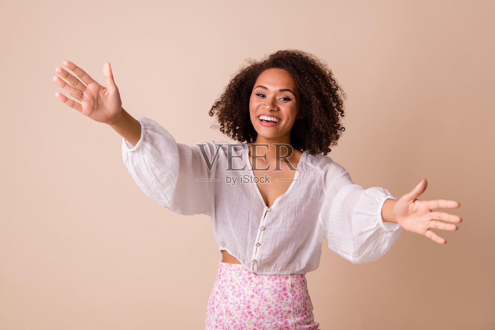 穿着白色衬衫、兴奋而闪亮的女孩，微笑着张开双臂，准备拥抱你，背景为米色。照片摄影图片