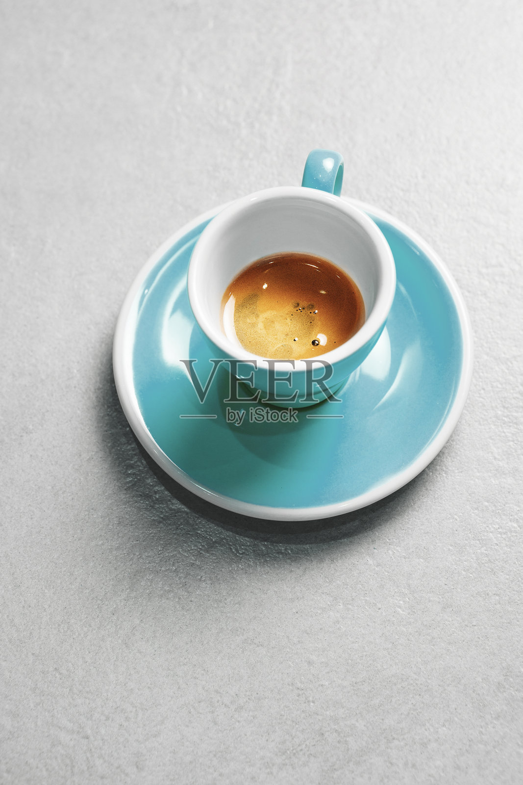 青绿色咖啡杯中注入浓郁的奶油意式咖啡，放在灰色桌面上照片摄影图片