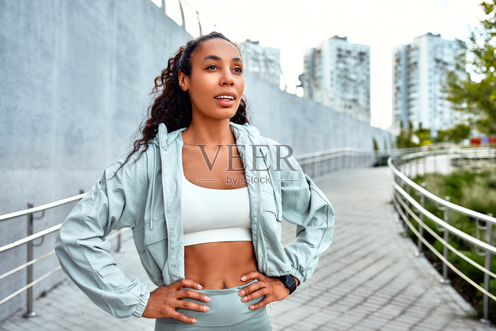 美丽的运动型成年女性穿着时尚现代的衣服，站着休息并在跑步后深呼吸，背景是道路和城市景观。留白空间。照片摄影图片