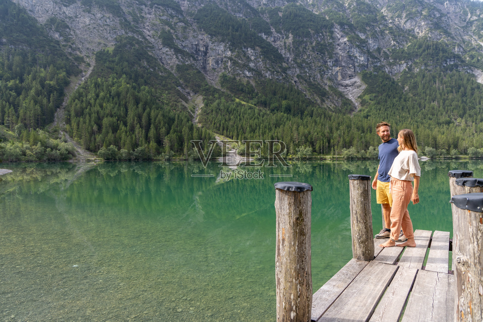 湖边码头上拥抱的情侣，背景是壮丽的山景照片摄影图片