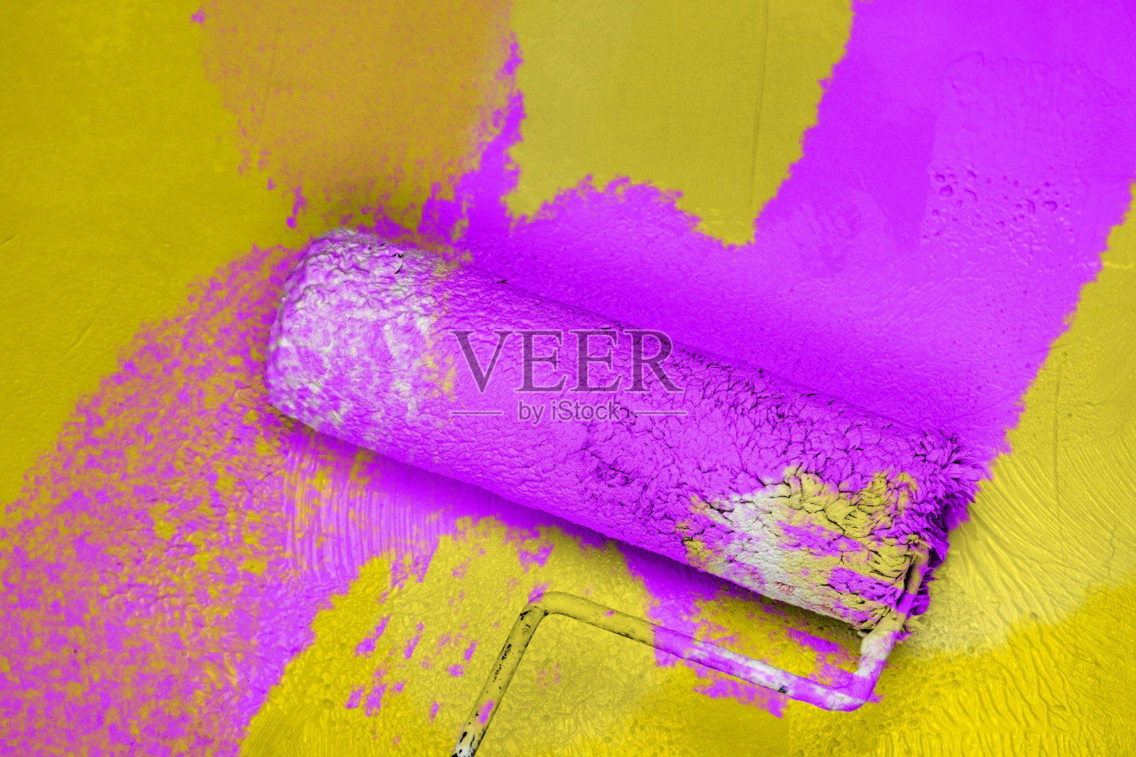 创意图形概念，油漆滚筒将新鲜的紫丁香色油漆涂抹在黄色混凝土墙上。家居装修、改进和改造的过程。留白空间。照片摄影图片