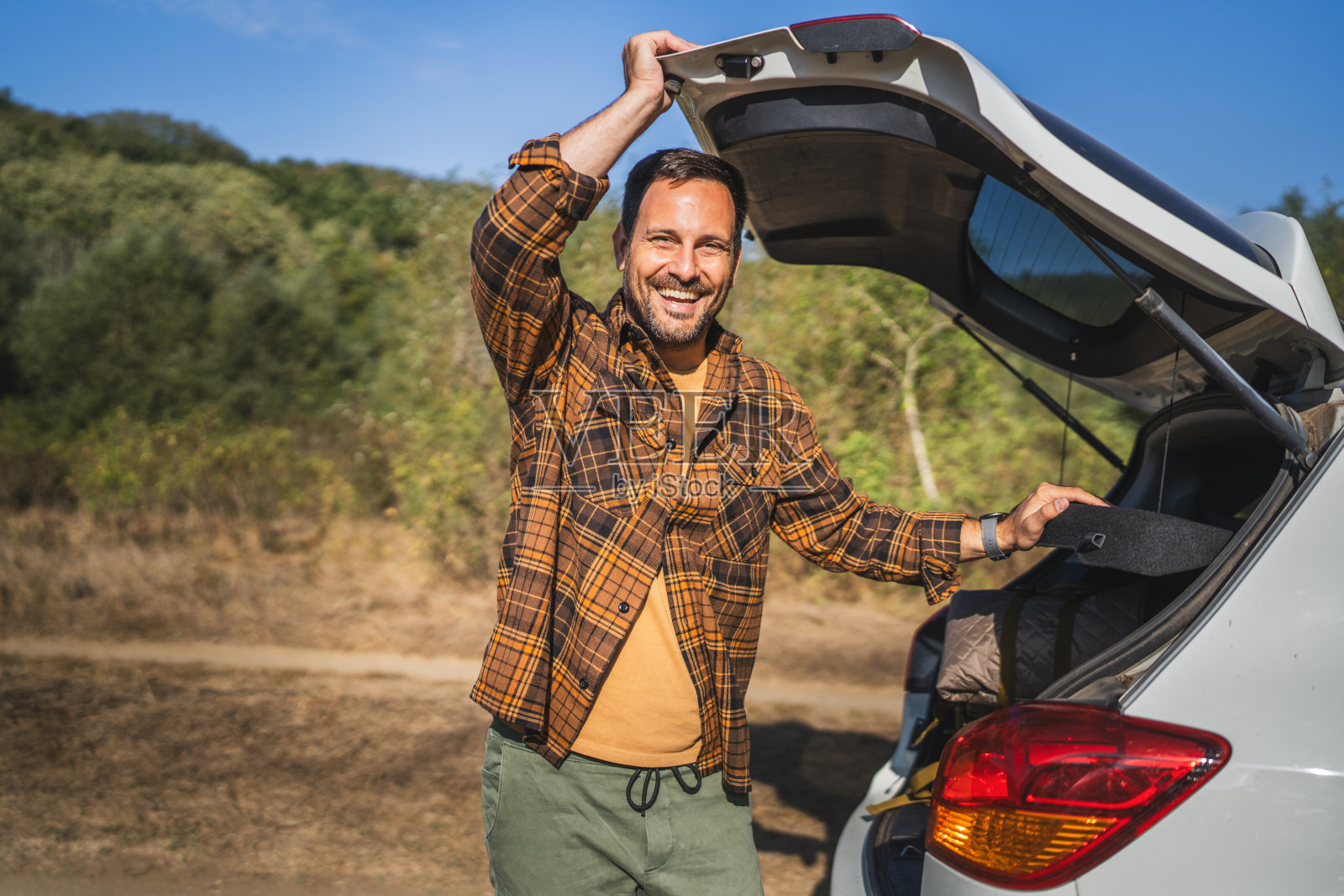 微笑的成年男性露营者靠近后备箱，准备迎接新的户外冒险照片摄影图片