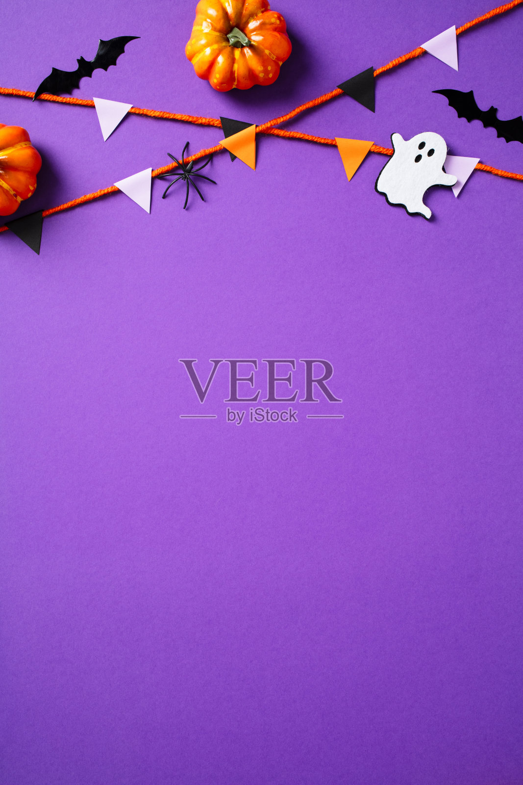 万圣节竖幅横幅，紫色背景上有彩旗、鬼魂、南瓜、蝙蝠和蜘蛛。俯视图，留白空间。照片摄影图片