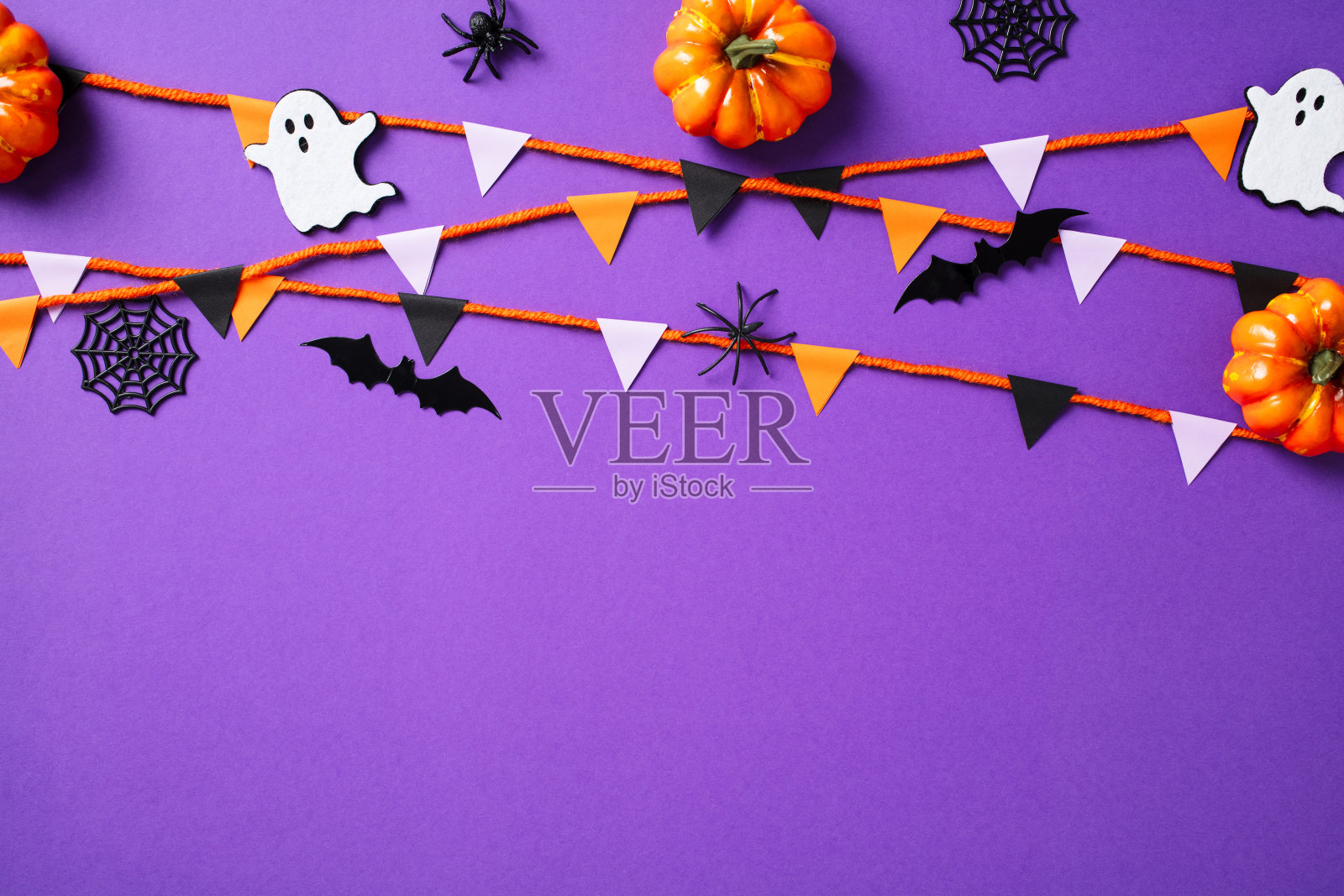 万圣节快乐的概念。紫色背景上平铺的南瓜、蜘蛛、鬼魂、蛛网和彩旗装饰。照片摄影图片