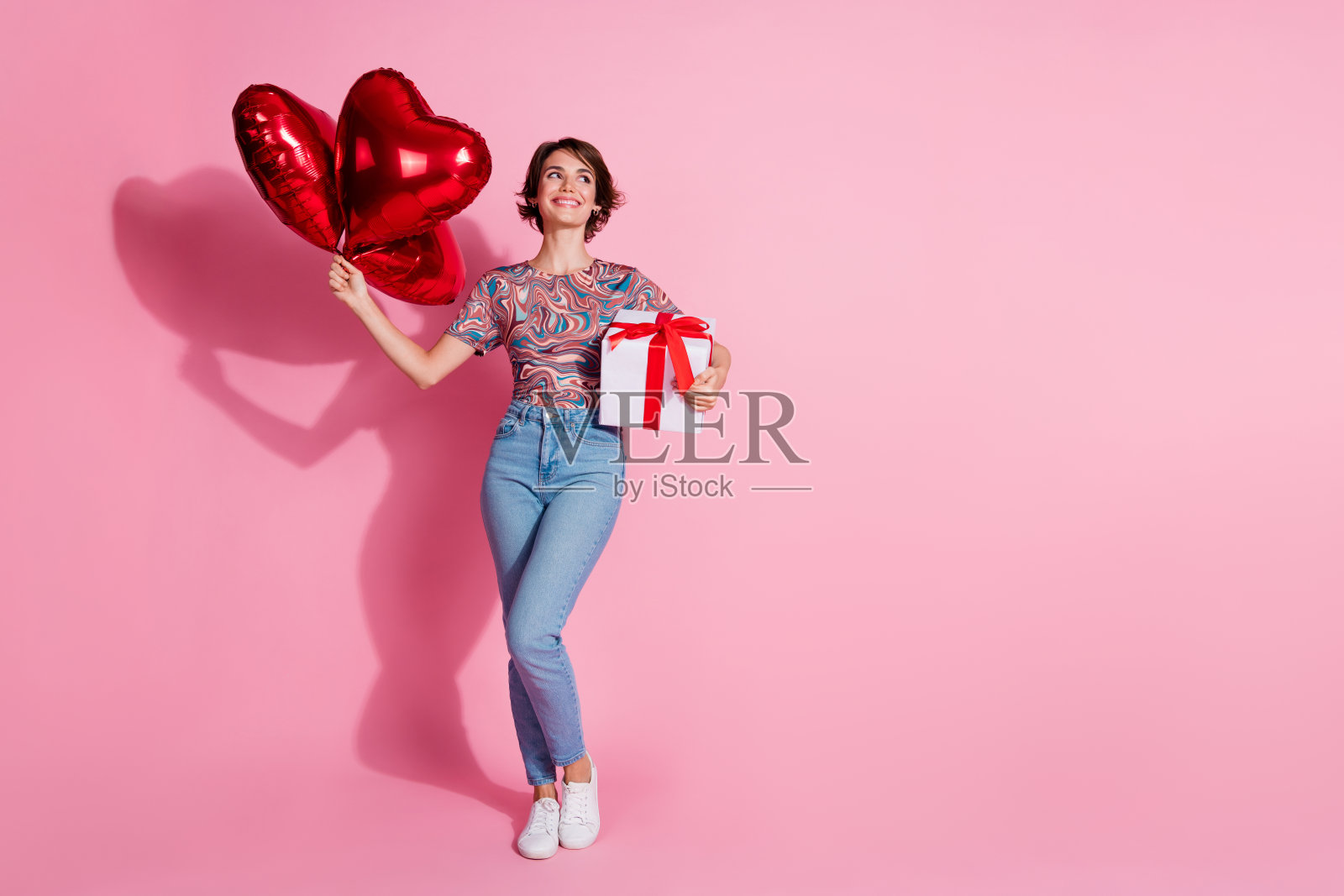 可爱的女孩穿着时尚的衣服，手里拿着礼物，望着空旷的空间，背景为粉色。照片摄影图片