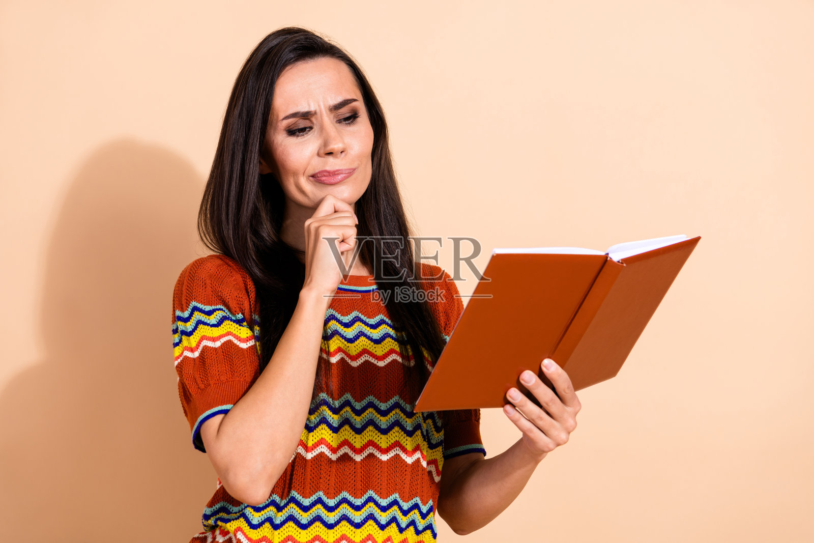 漂亮年轻女士穿着T恤，独自一人阅读书籍，思考，背景为米色。照片摄影图片