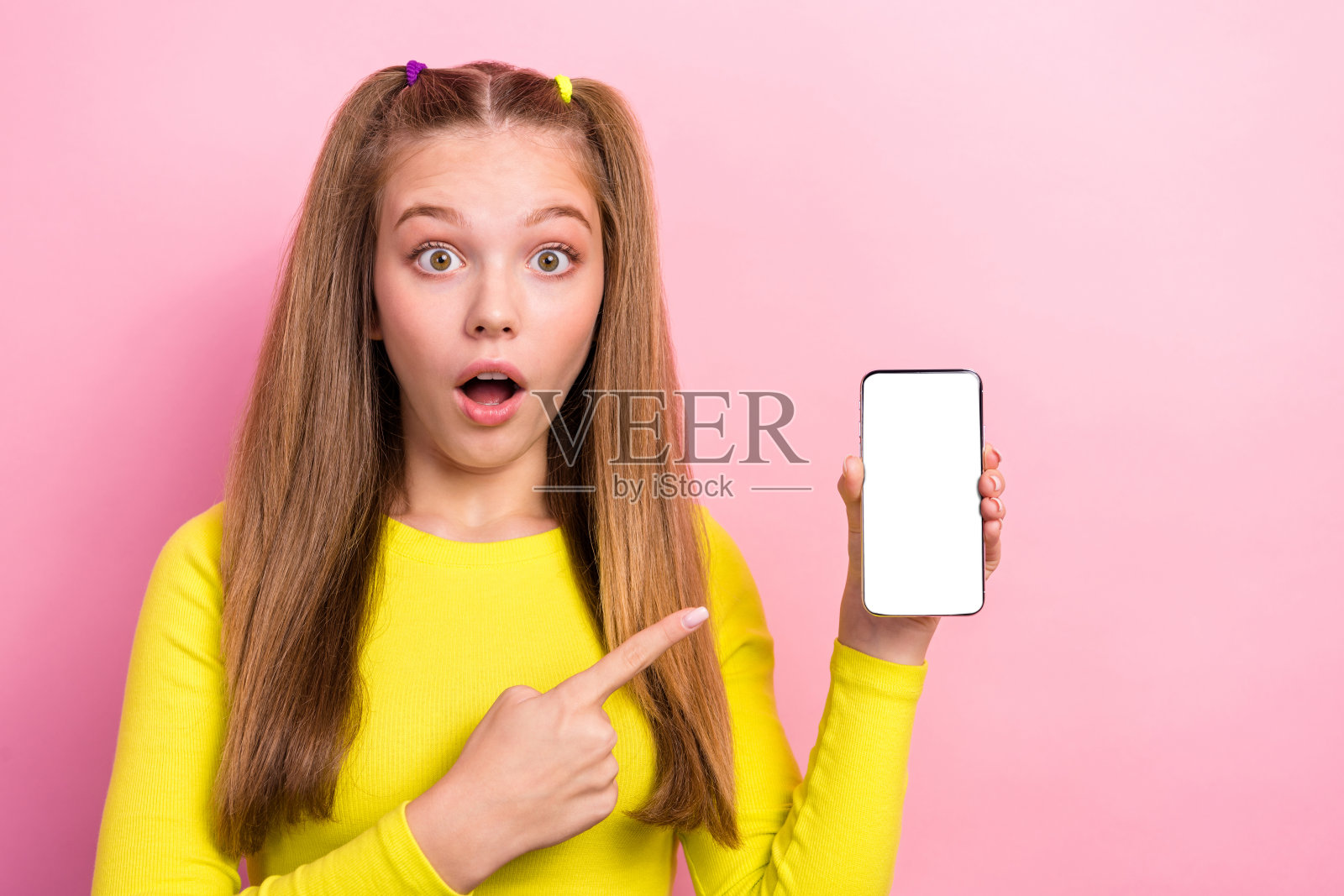 惊讶的迷人少女手持现代小工具，因低价而感到惊喜，背景为空白的粉色。照片摄影图片