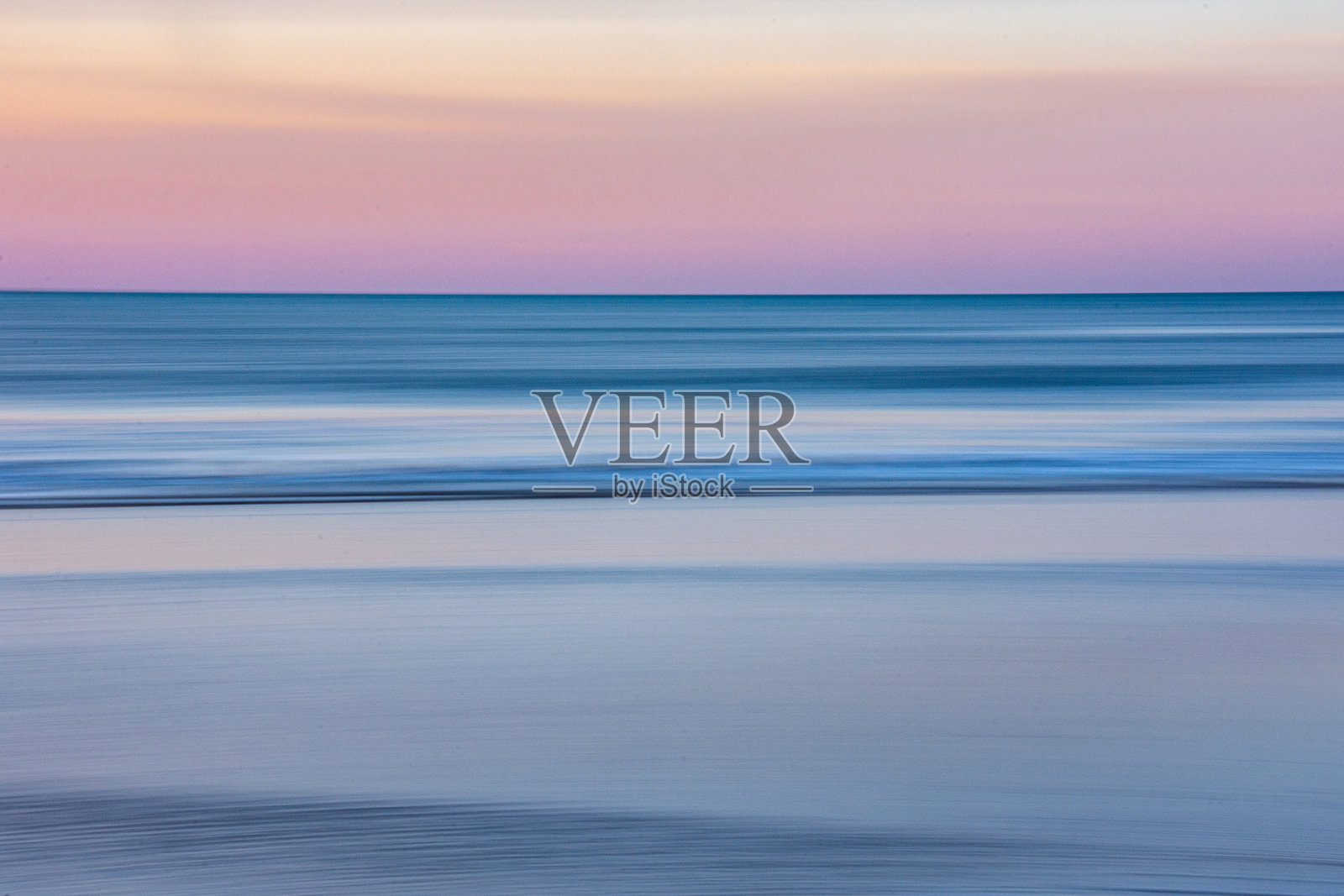 长时间曝光的海滩日落，捕捉到色彩的渐变。拍摄时移动了相机，产生了模糊效果。照片摄影图片