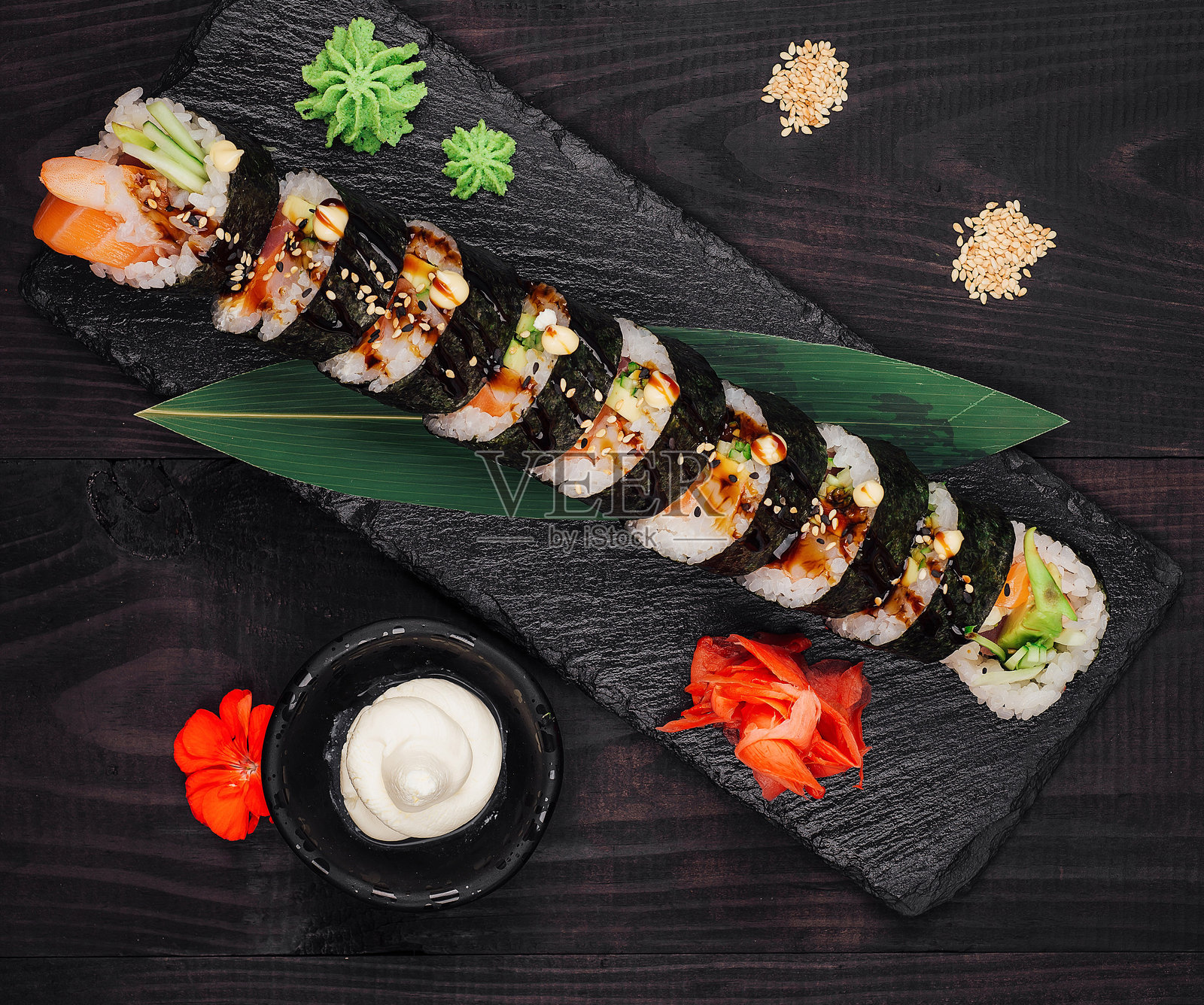 黑色石板上摆放的寿司卷，背景为深色木材。照片摄影图片