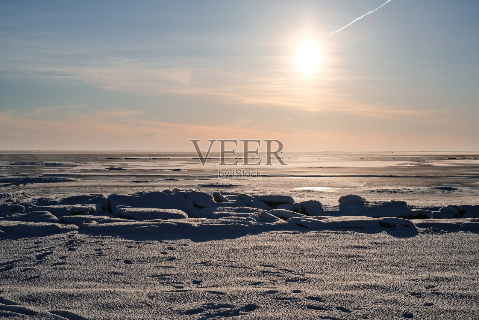 一片冰冻的海洋。背景中太阳正在落下。天空是蓝色的，太阳高挂在空中。照片摄影图片