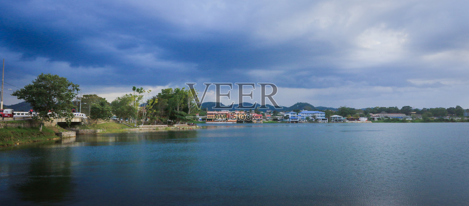在危地马拉弗洛雷斯的湖边，阴云密布的天空下，沿岸有色彩鲜艳的建筑，景色如画。照片摄影图片