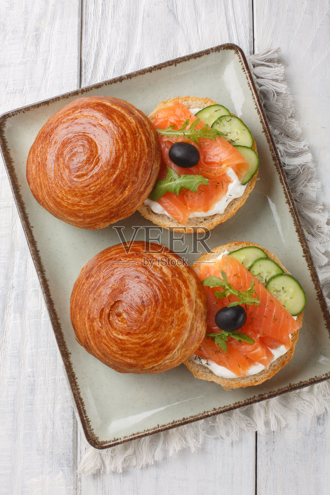 酥脆的泡芙面团三明治，夹有熏三文鱼、奶油奶酪、黄瓜和橄榄，特写在盘子上。垂直俯视。照片摄影图片