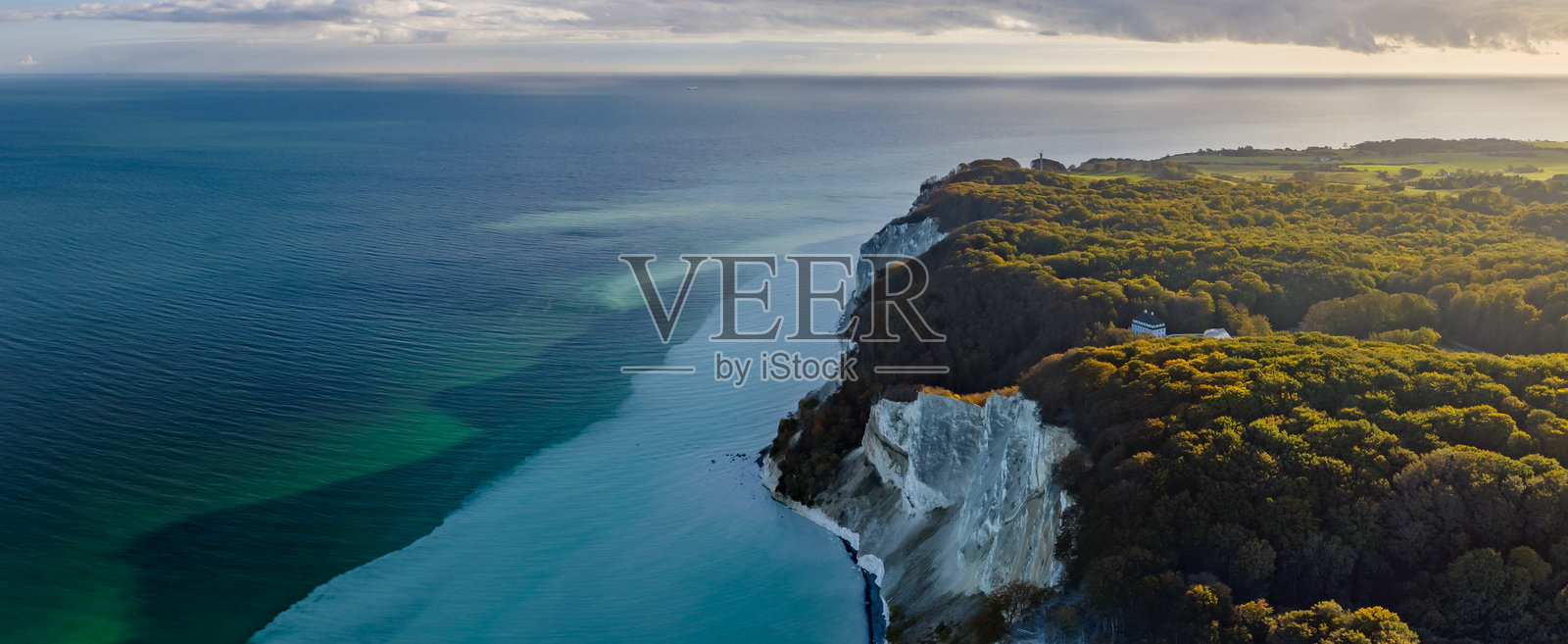 白色悬崖、茂密森林和经典斯堪的纳维亚建筑风格的建筑俯瞰在平静的蓝色海洋背景下。莫恩斯克林特的白垩悬崖风景。照片摄影图片