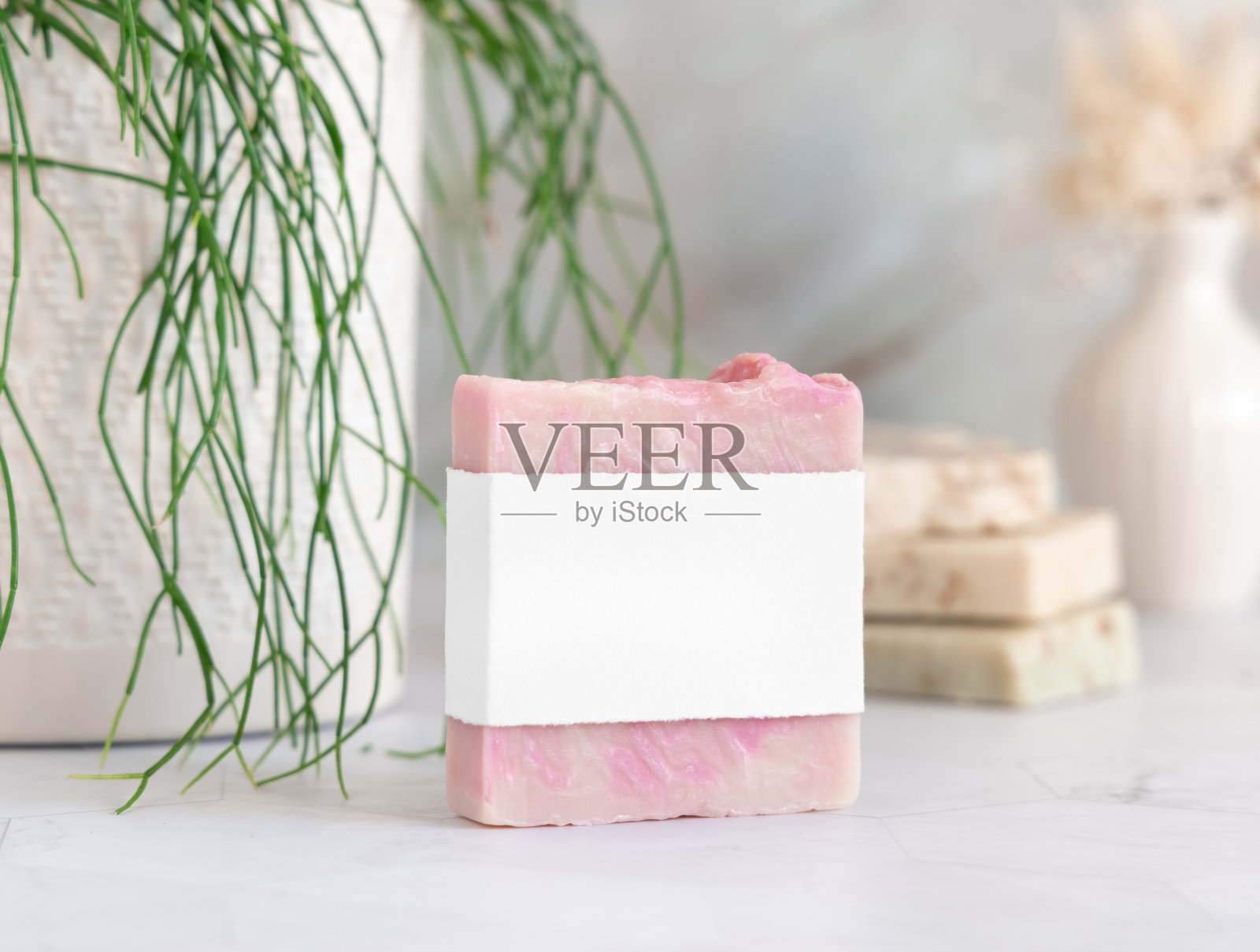 大理石台面上放着一块带空白标签的香皂，旁边有绿色植物，特写，化妆品样机照片摄影图片