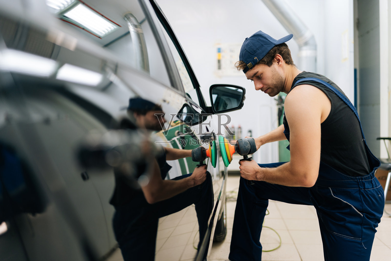 机械工人在汽车修理店里，戴着帽子，正在用抛光机对豪华车的车门进行抛光。专业的汽车喷漆技师正在使用汽车抛光机。照片摄影图片