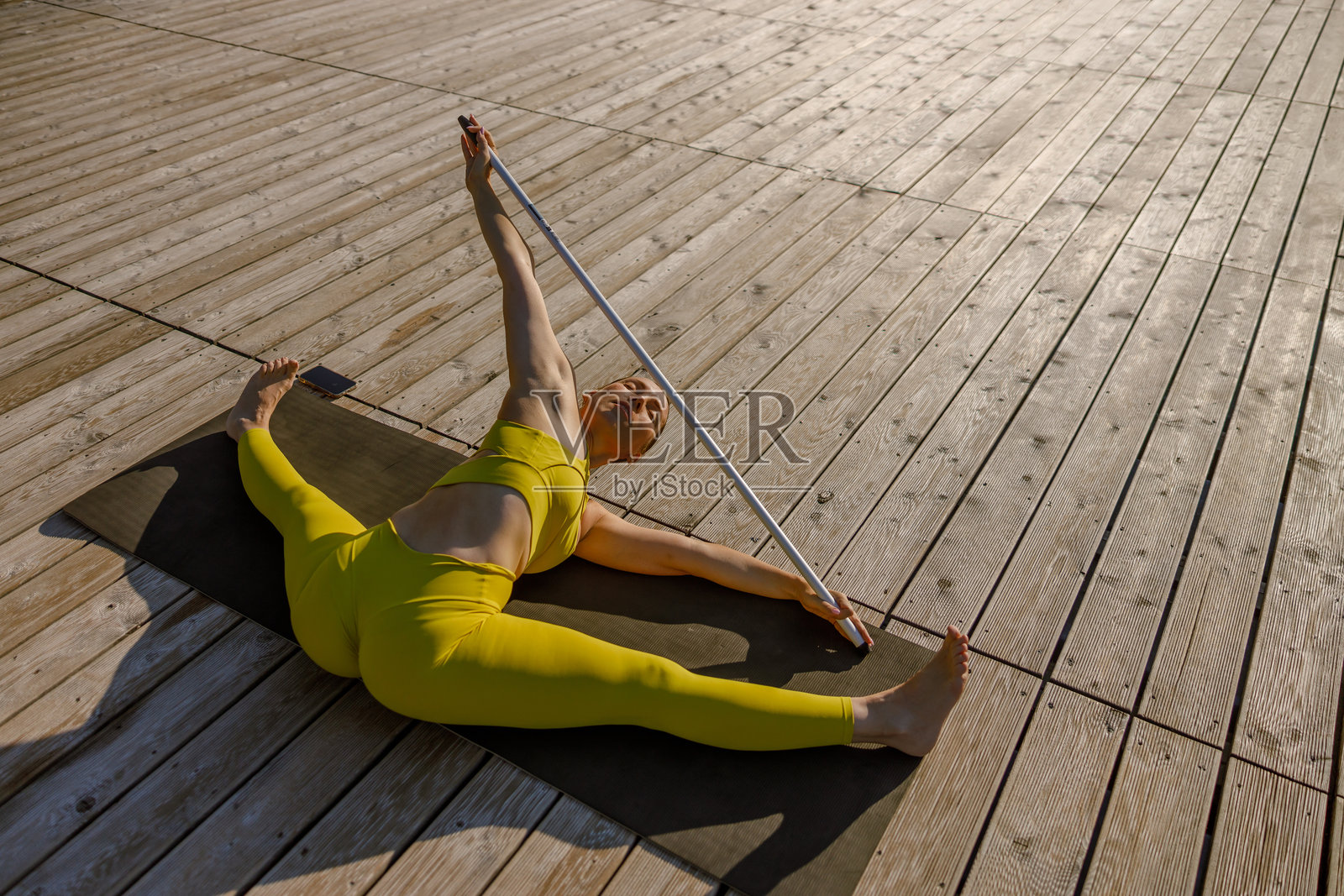 在美丽的日出甲板上使用拉伸杆进行灵活的瑜伽姿势照片摄影图片