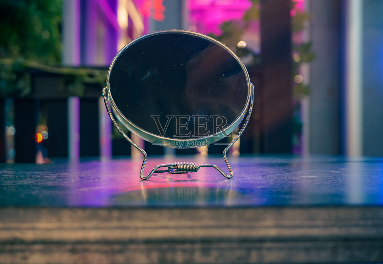 一面靠在金属表面上的镜子的特写，背景有霓虹灯光。照片摄影图片