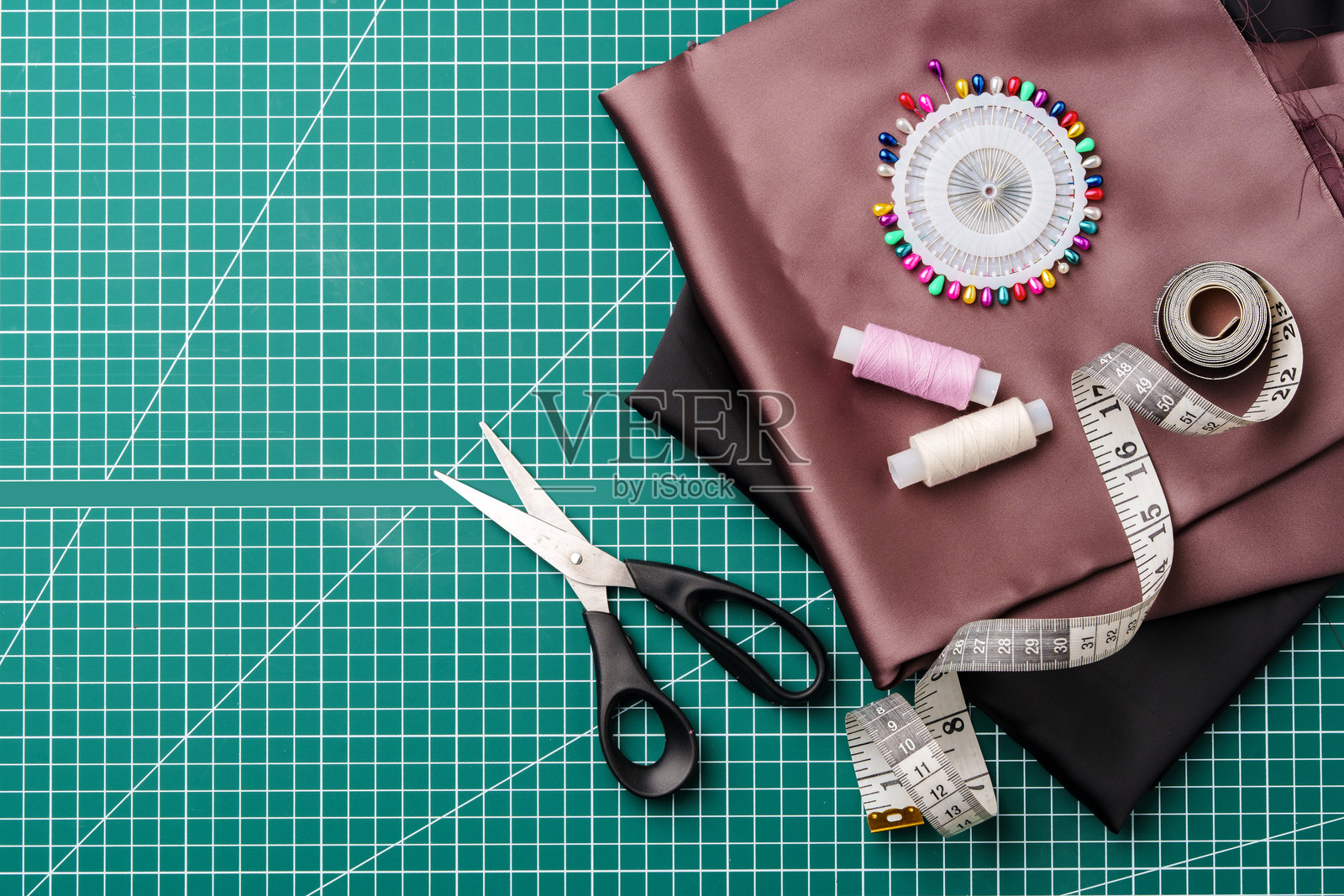 缝纫用的工艺用品，放在绿色切割垫上，包括布料、剪刀和测量工具照片摄影图片